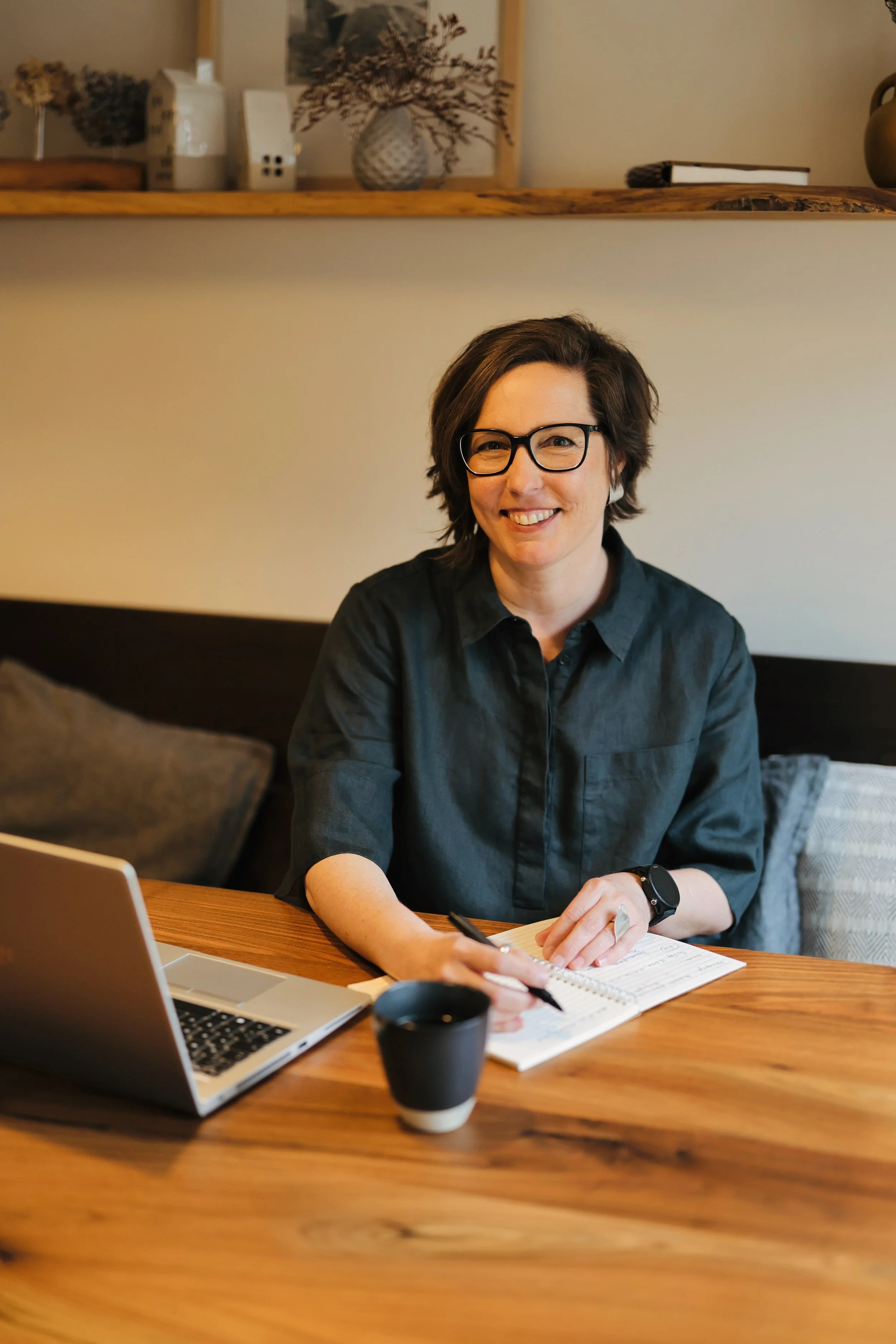 Julia Fieweger sitzt beim Lektorat  von Reiseliteratur oder einer Biografie am Tisch vor ihrem Laptop und notiert etwas im Notizbuch