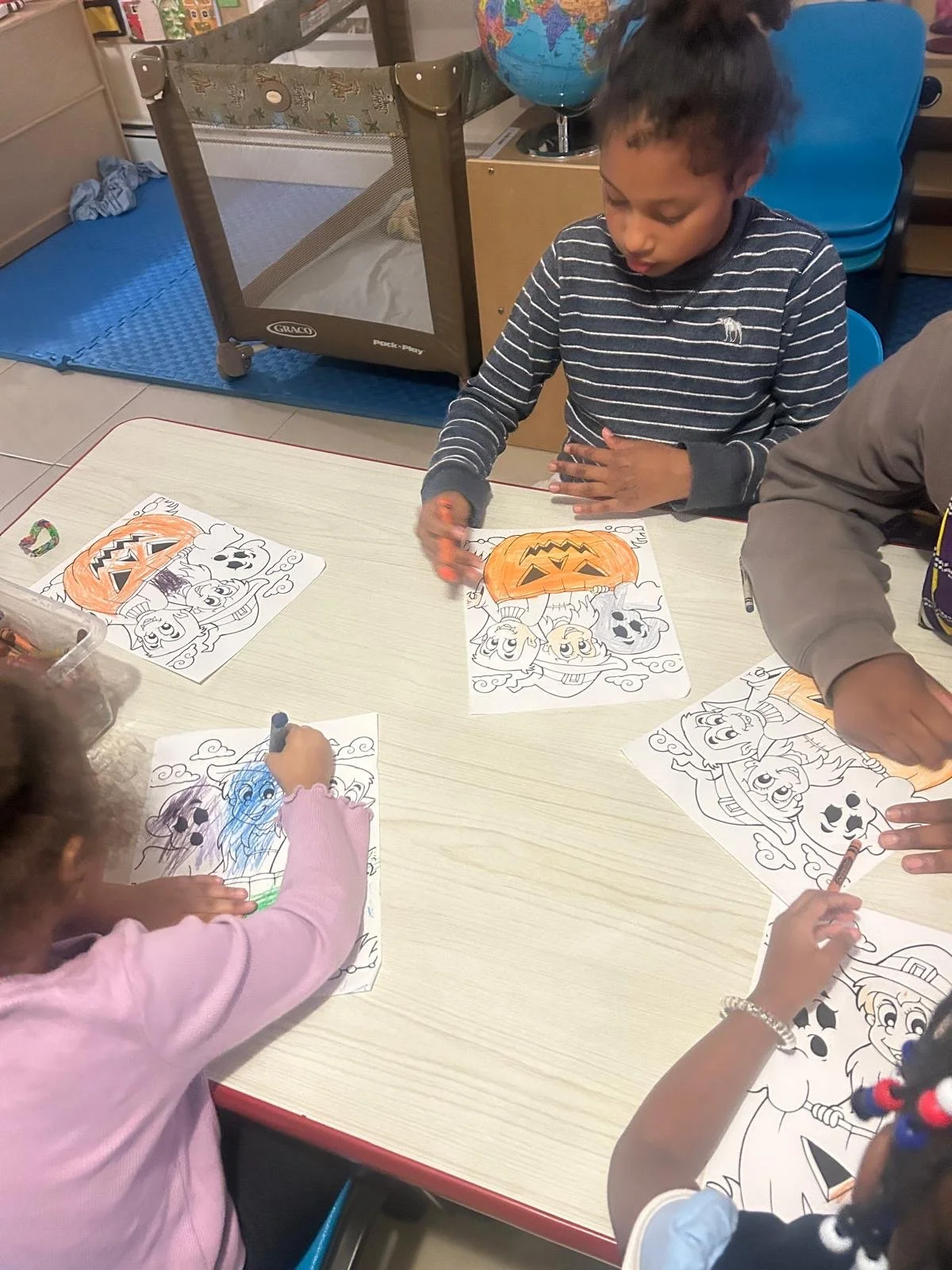 Children coloring Halloween themed pictures at a table, featuring pumpkins, witches, and ghosts.