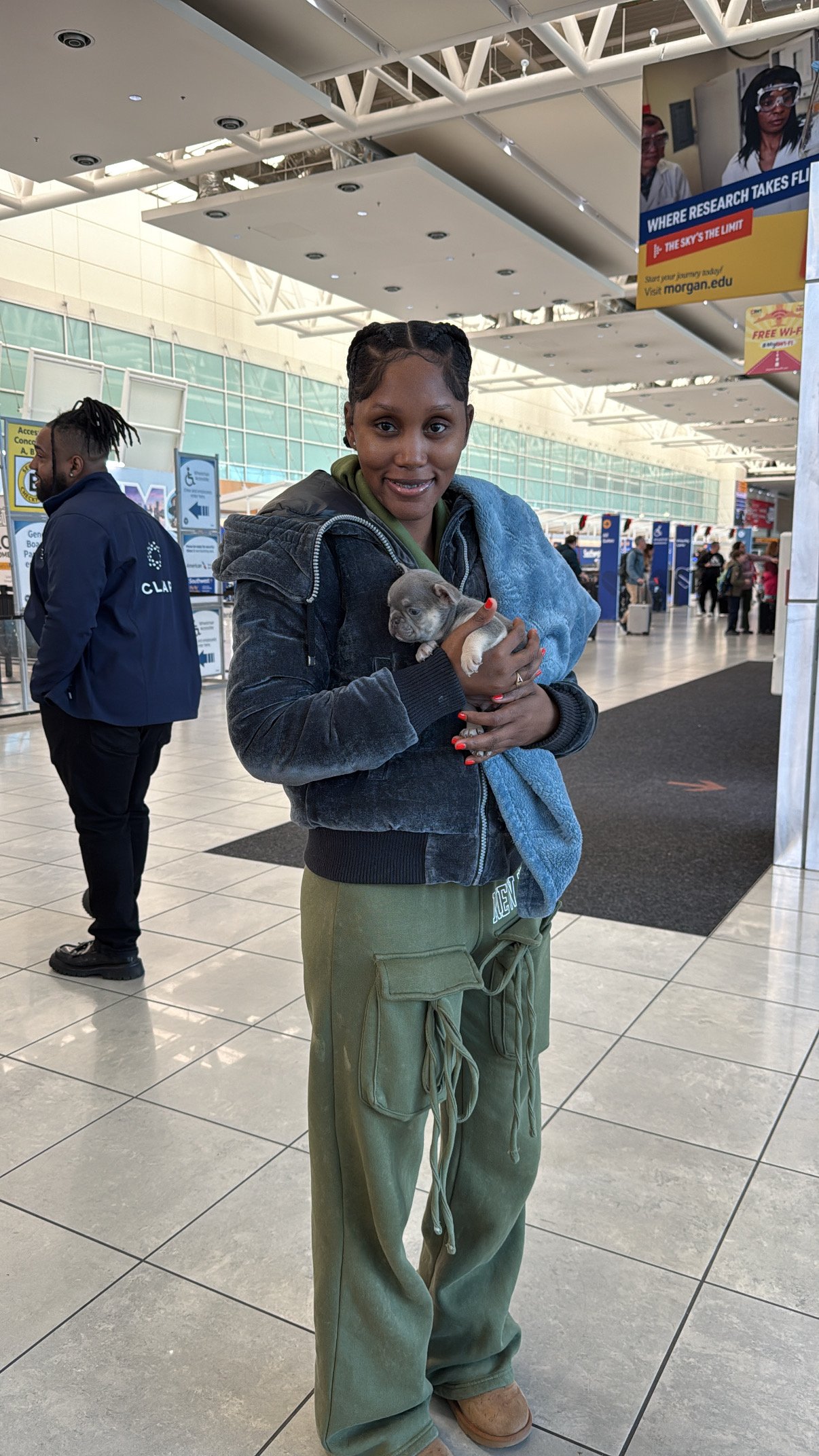 A woman holding a small puppy in an airport terminal