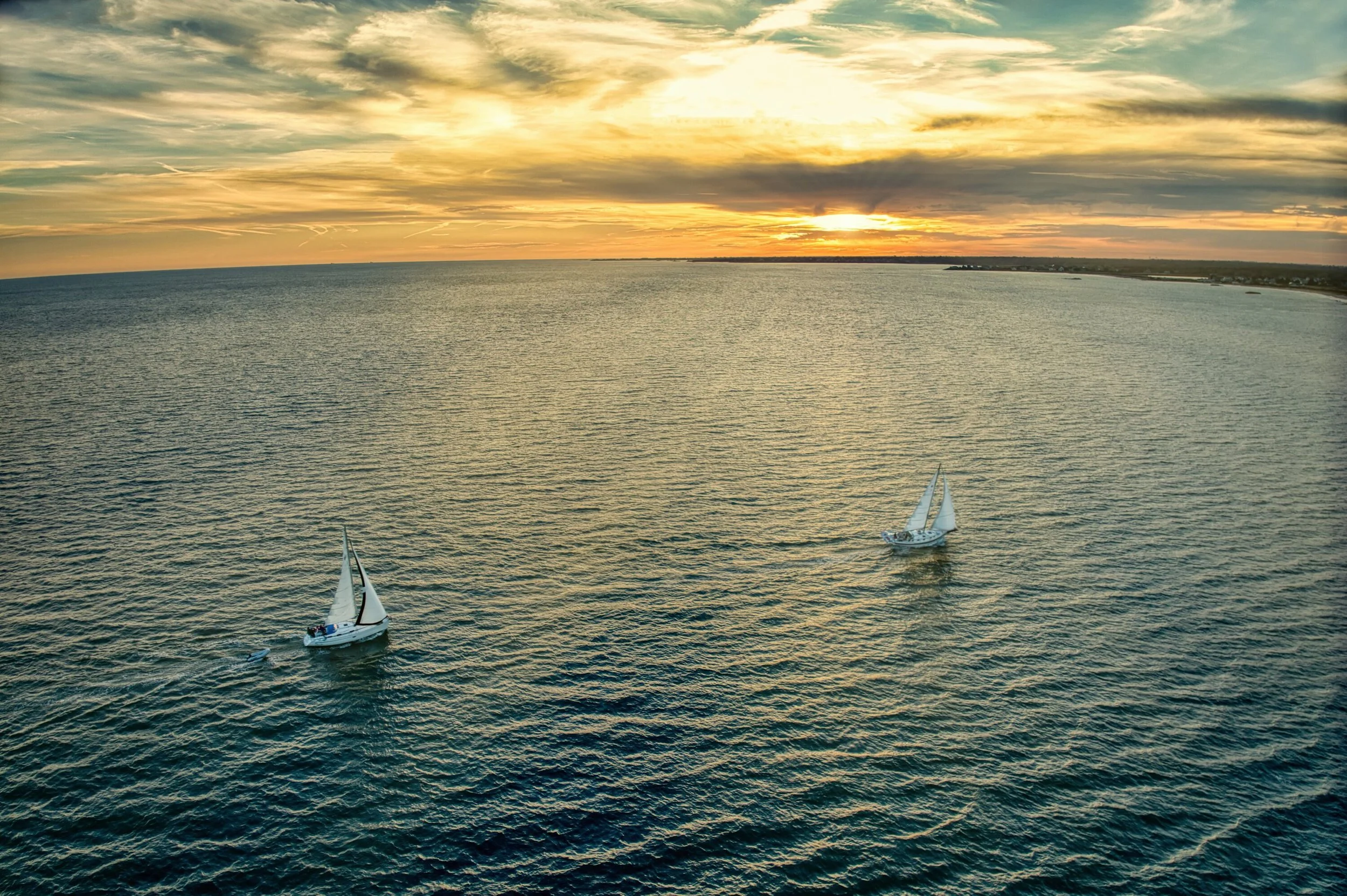 Two sailboats on calm water at sunset with a partly cloudy sky and distant horizon of Buzzards Bay in Westport, Massachusetts. 