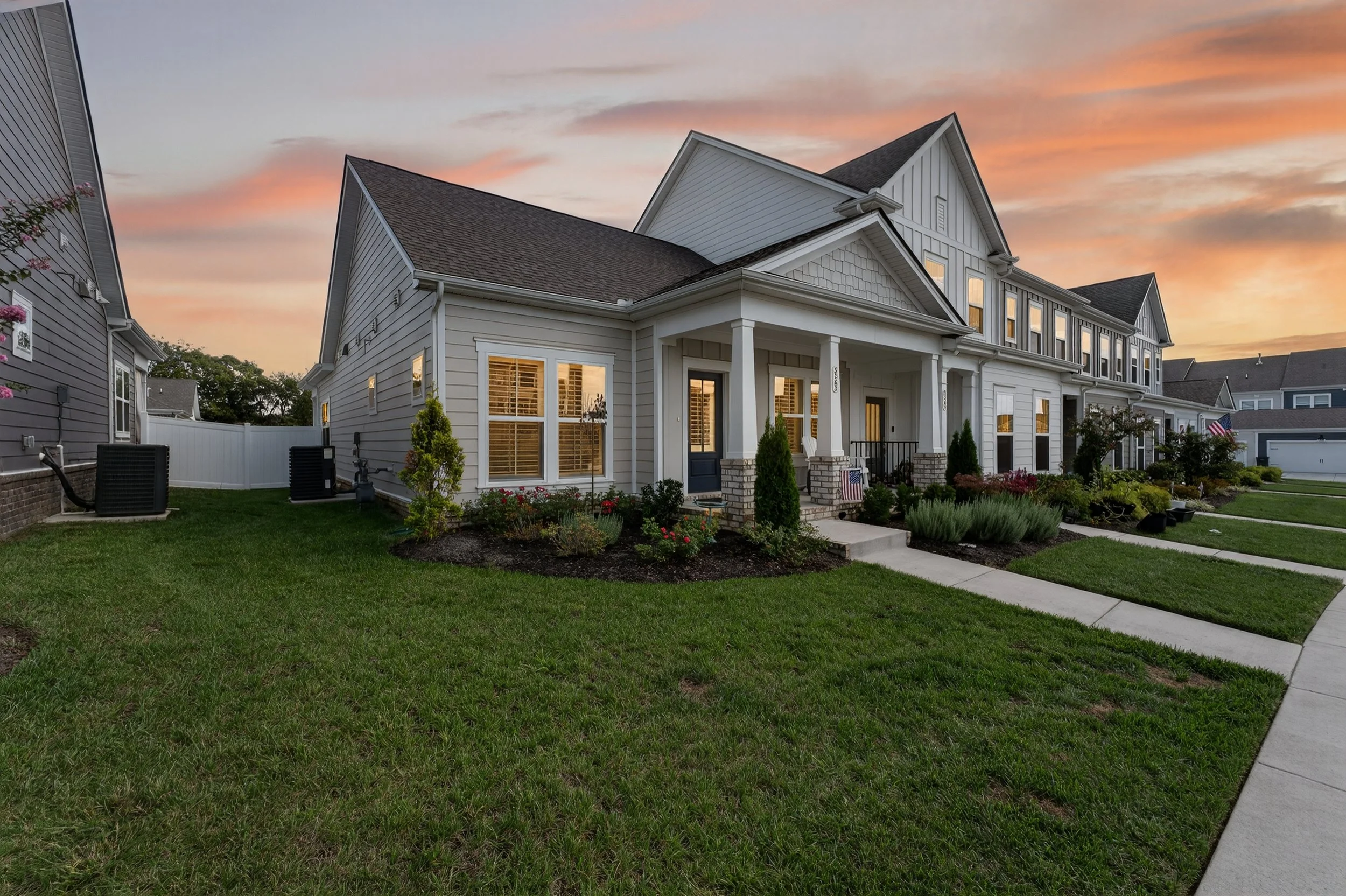 Front view of a large white house with a porch, multiple windows, and a well-manicured lawn during sunset.
