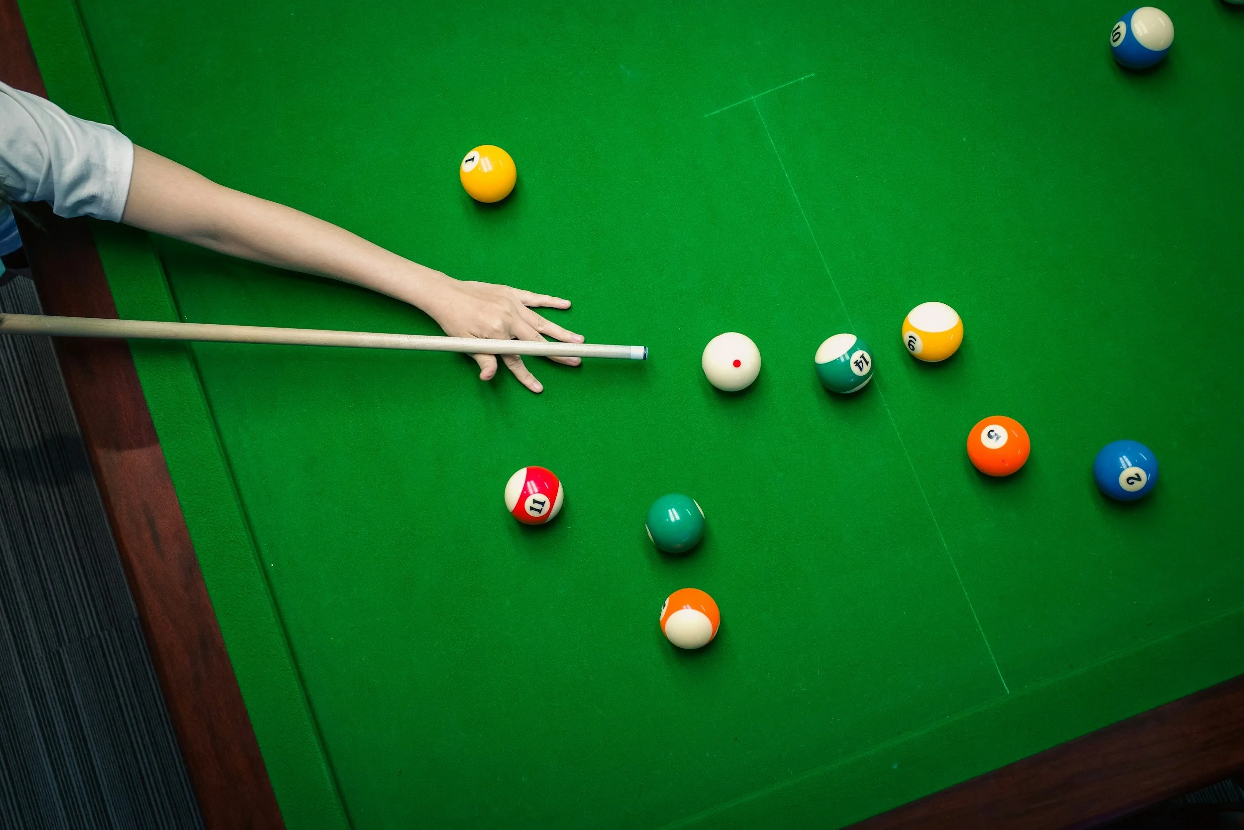 Person spielt Billard, mit mehreren bunten Billardkugeln auf grünem Tischtuch, einige Kugeln sind bereits versetzt.