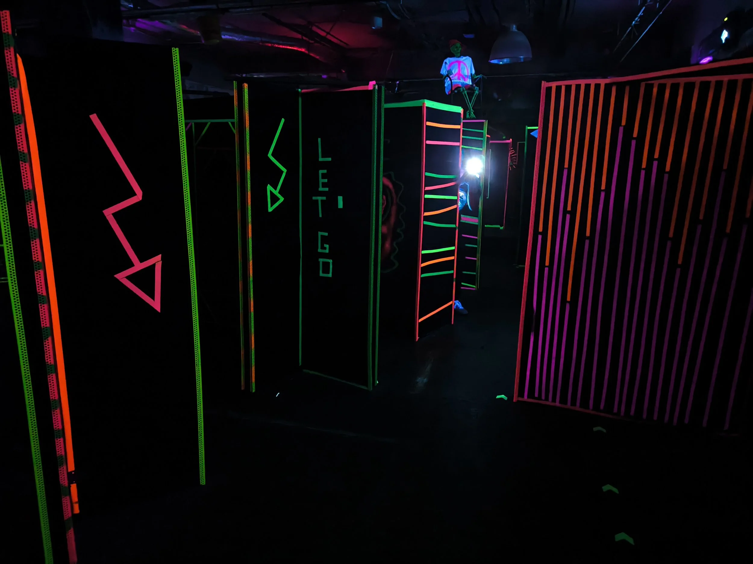 Neonlichter und Linien im Dunklen, mit einem auf einem der Höhlen sitzenden Puppen, die ein Peace-Zeichen zeigt.