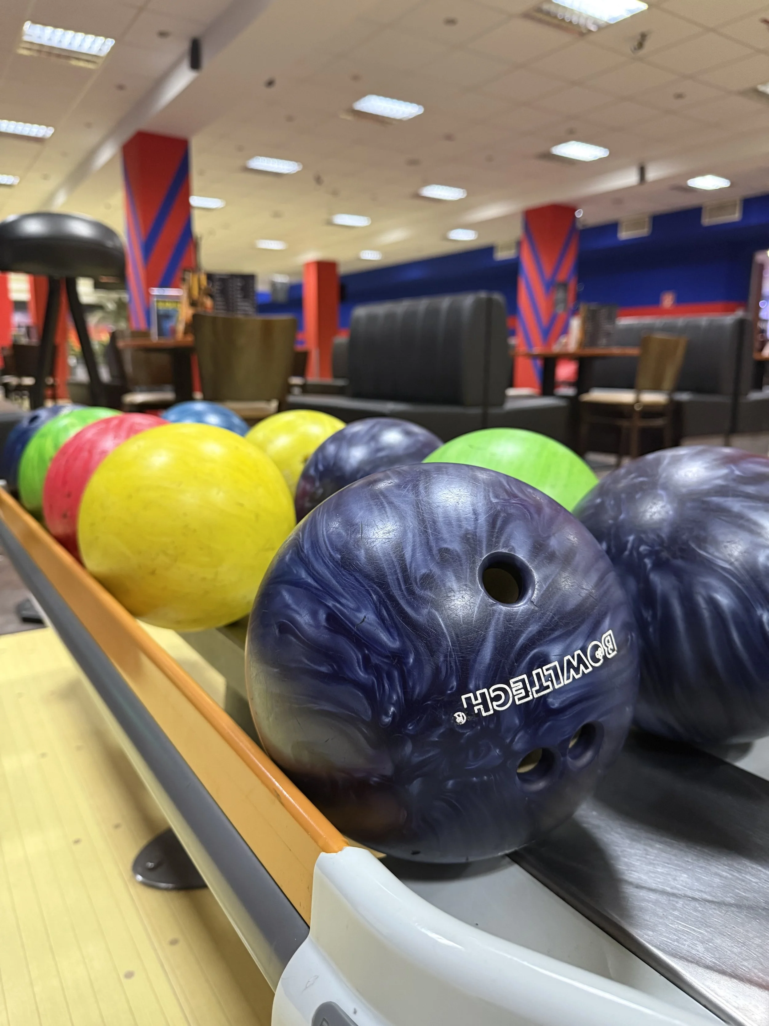 Mehrfarbige Bowlingkugeln auf einem bowlingbahn. Hintergrund innen im Bowlingcenter mit Tischen und Sitzgelegenheiten.