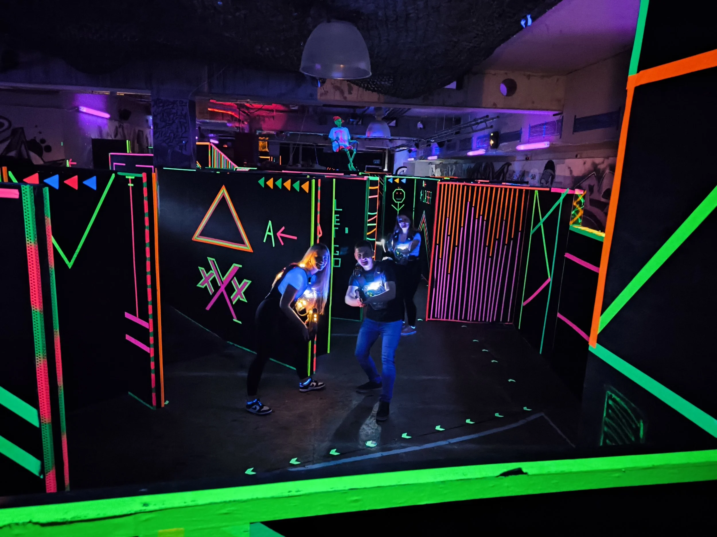 Menschen in einem Schwarzlicht-Labyrinth mit leuchtenden, neonfarbenen Designs und Figuren, die sich für eine Gruppeaufnahme positionieren.