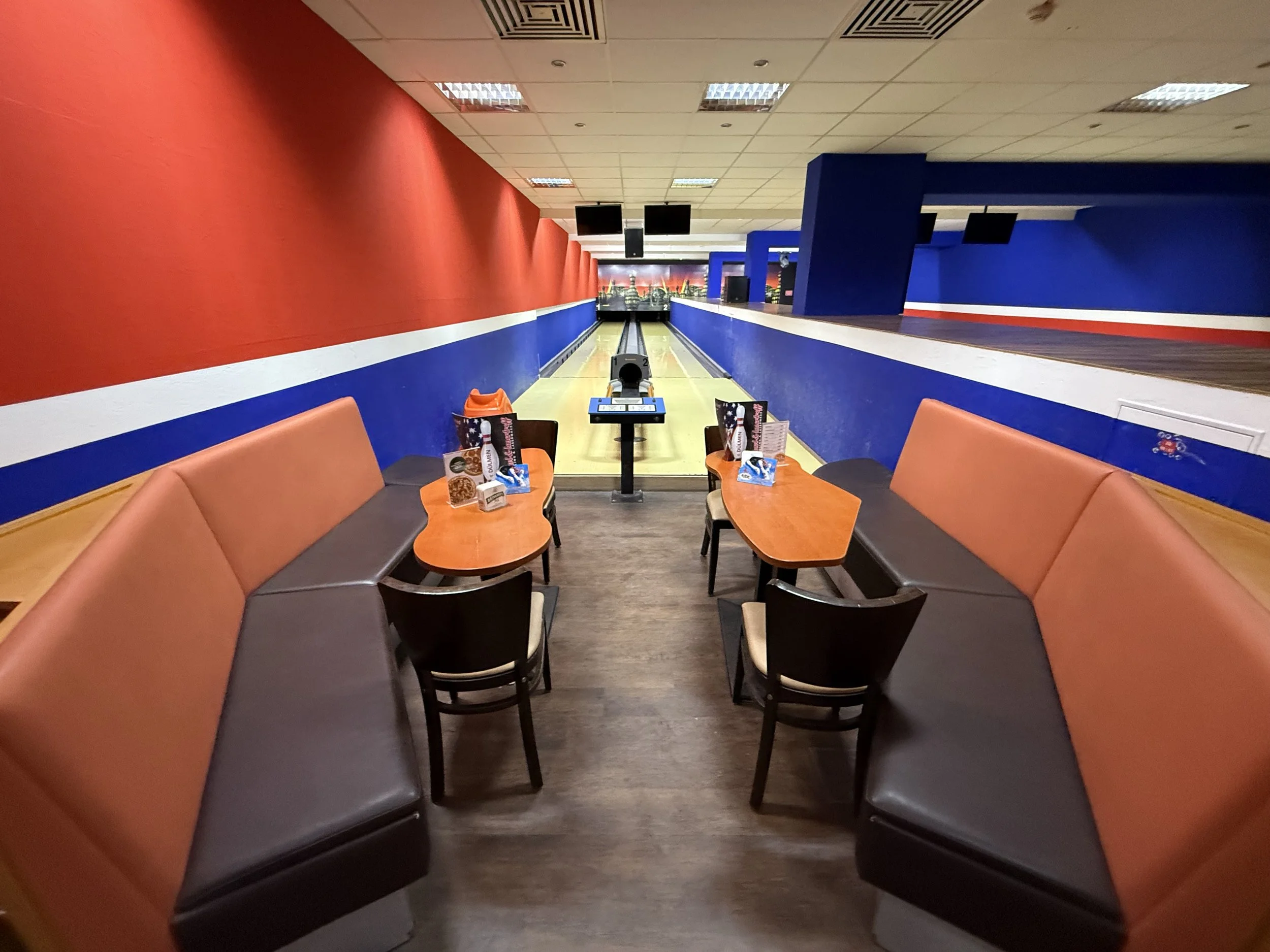 Eine leere Bowlingbahn in einer Bowlinghalle mit Sitzbereichen, Lichtern und einem Score-Tisch.
