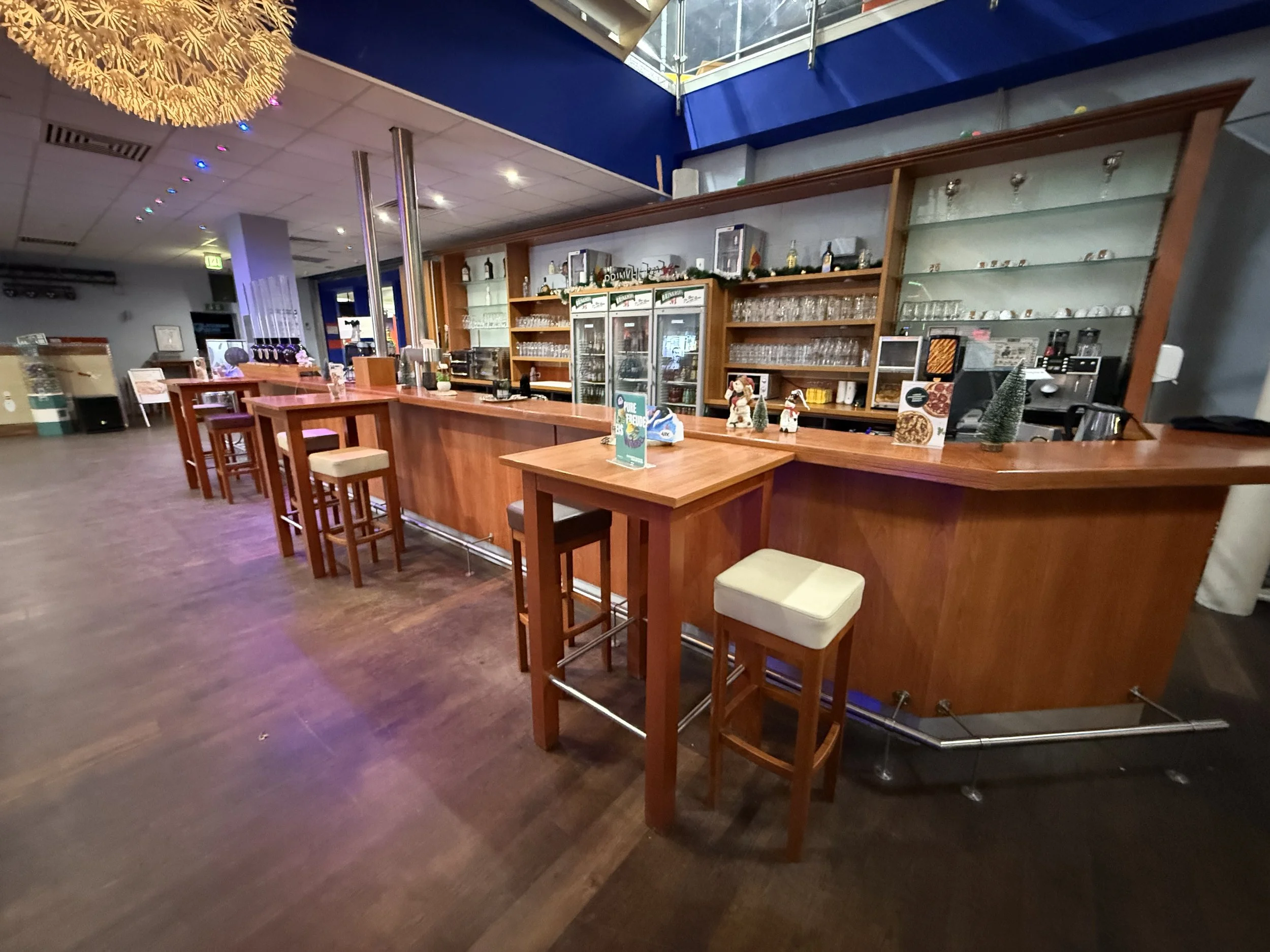 Unppbar der Barbereich in einem Café oder Restaurant mit Holztheke, Barhockern, Glasregalen und Dekorationen.