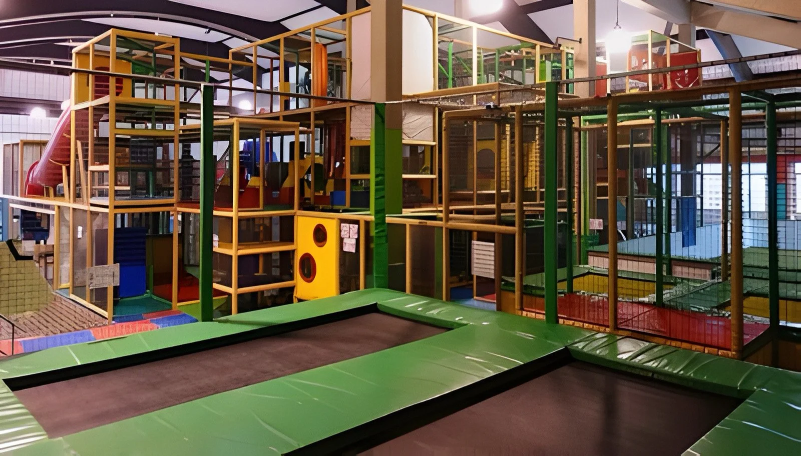 Innenansicht eines Kletterparks mit verschiedenen bunten Kletterstrukturen, Rutschen und Trampolinen.