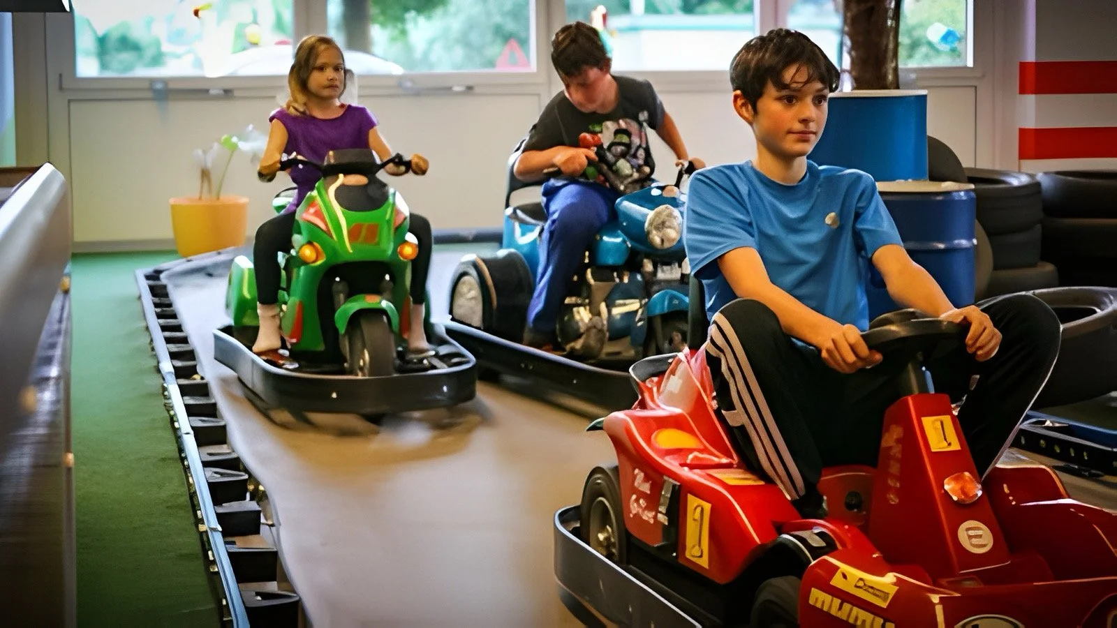 Drei Kinder fahren auf Miniauto- und Motorrädern in einer Indoor-Spielhalle.