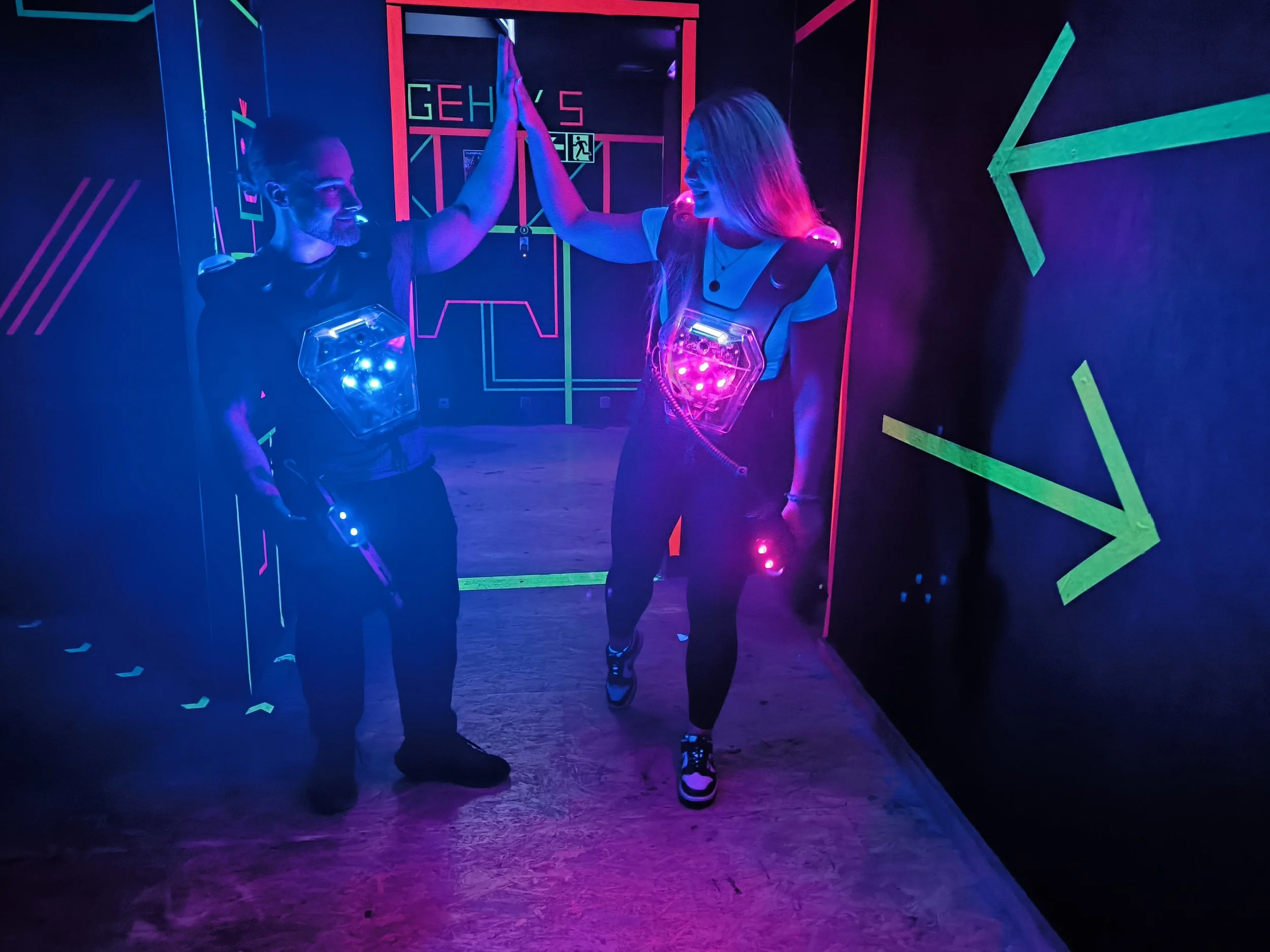 Zwei Personen in einem LED-aktivierten Raum, die sich high-five geben, mit Laserpointern und leuchtenden LEDs auf ihrer Kleidung.