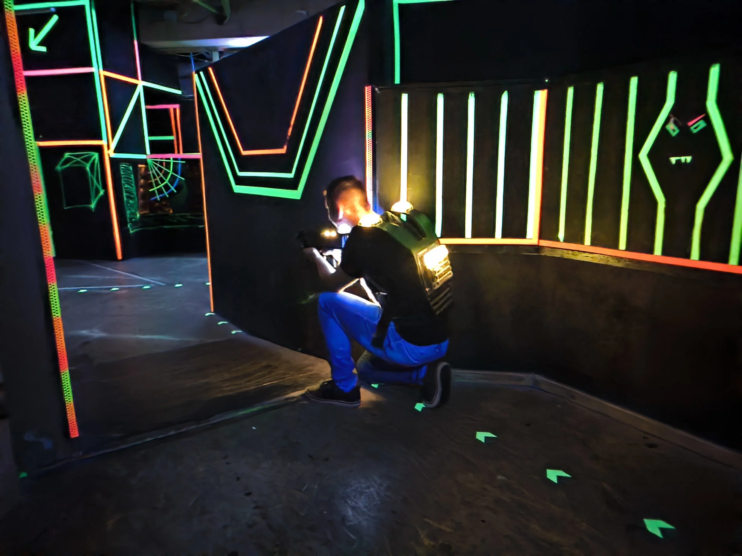 Person mit Laser-Tag-Ausrüstung in einer Neon-beleuchteten Spielhalle.