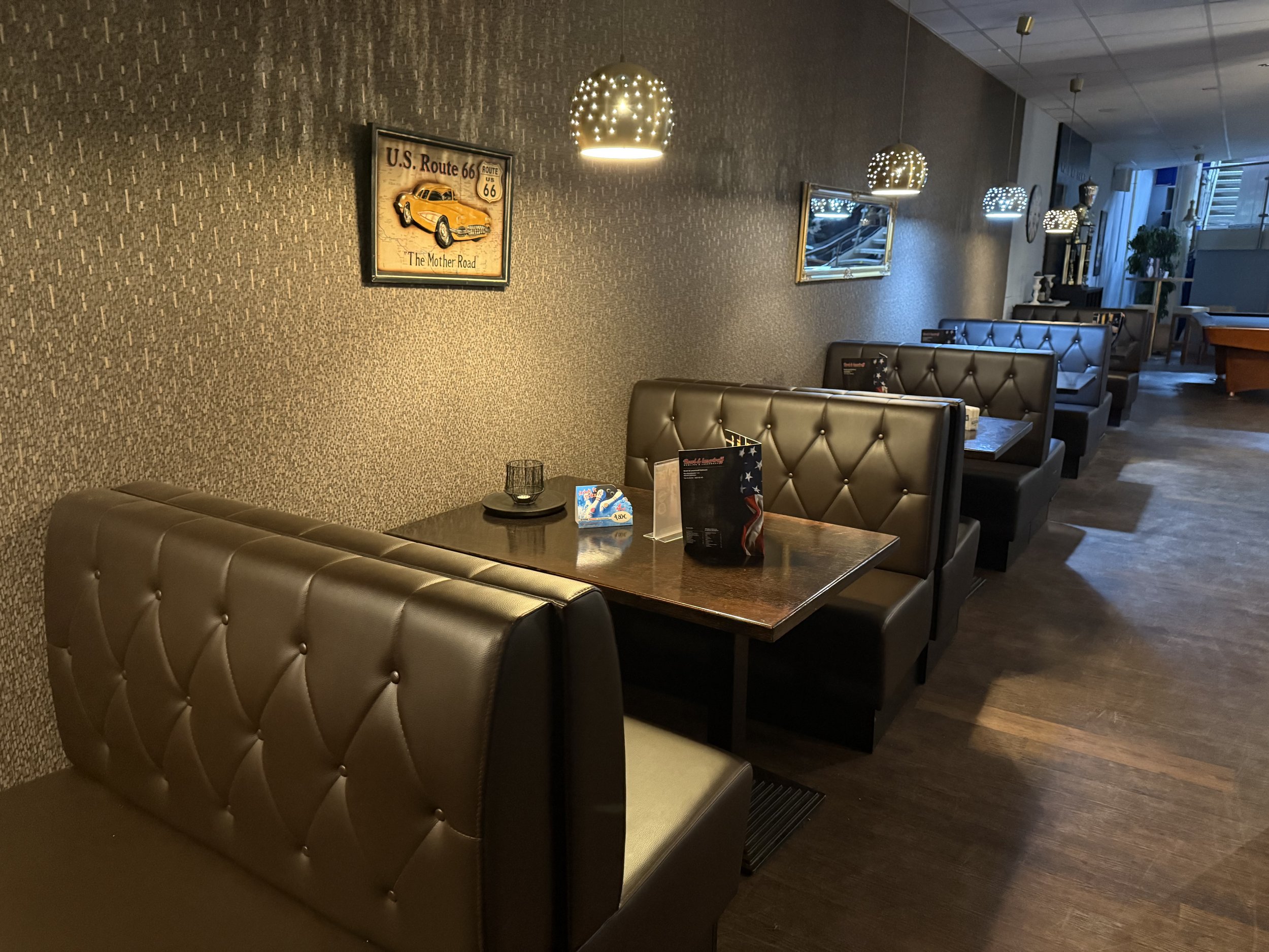 Innenraum eines Restaurants mit dunkelbraunen Sitzecken, Wanddekoration und indirekter Beleuchtung.