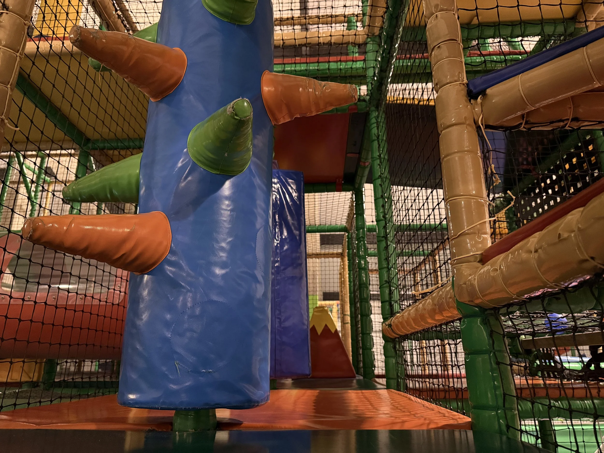 Innenansicht eines kindgerechten Spielbereichs mit bunten Kissen und Rutschen, umgeben von Gittern.