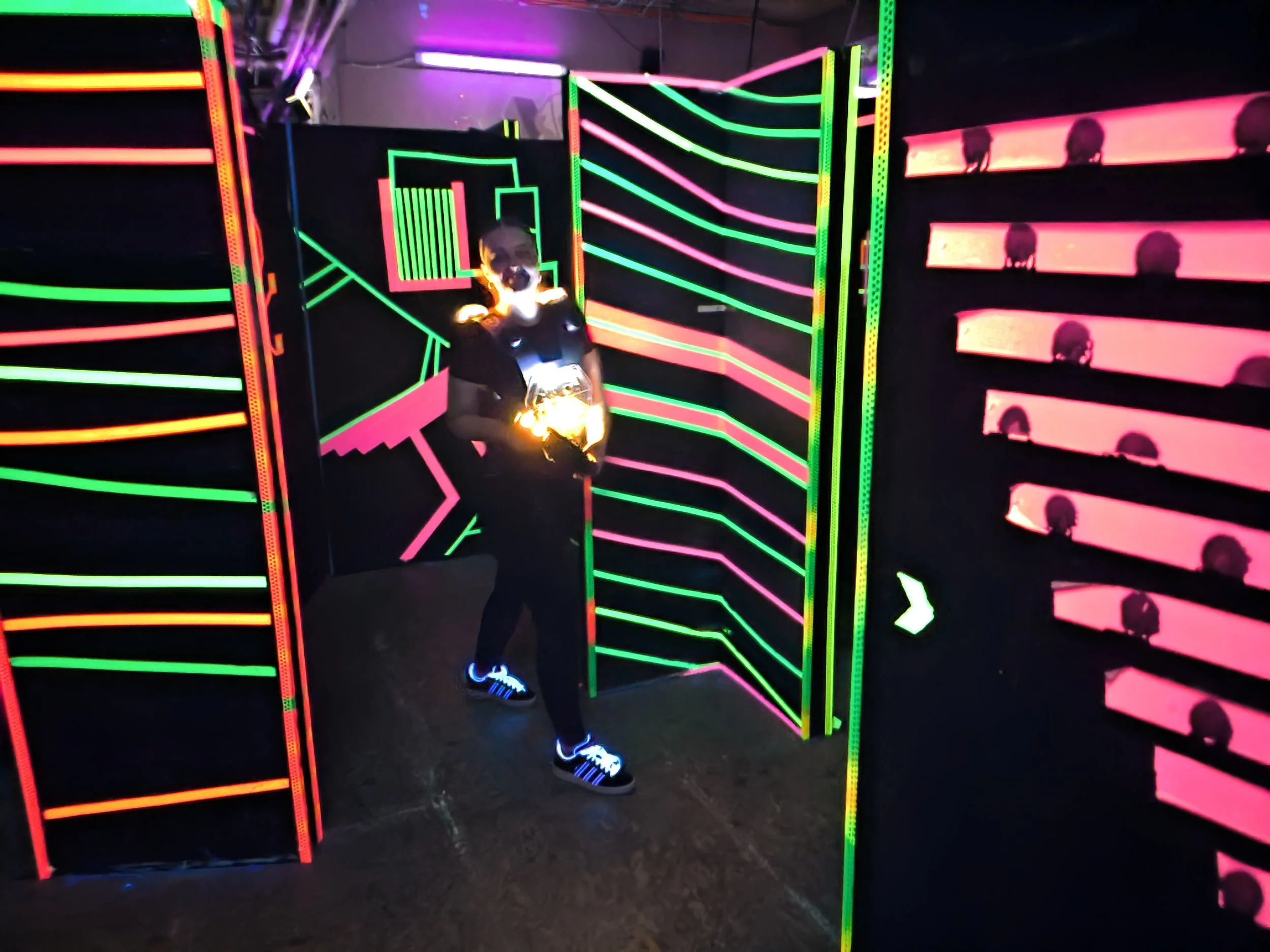 Eine Person in einem dunklen Raum mit Neonlichtern, die vor einer Wand mit leuchtenden, bunten Mustern steht.