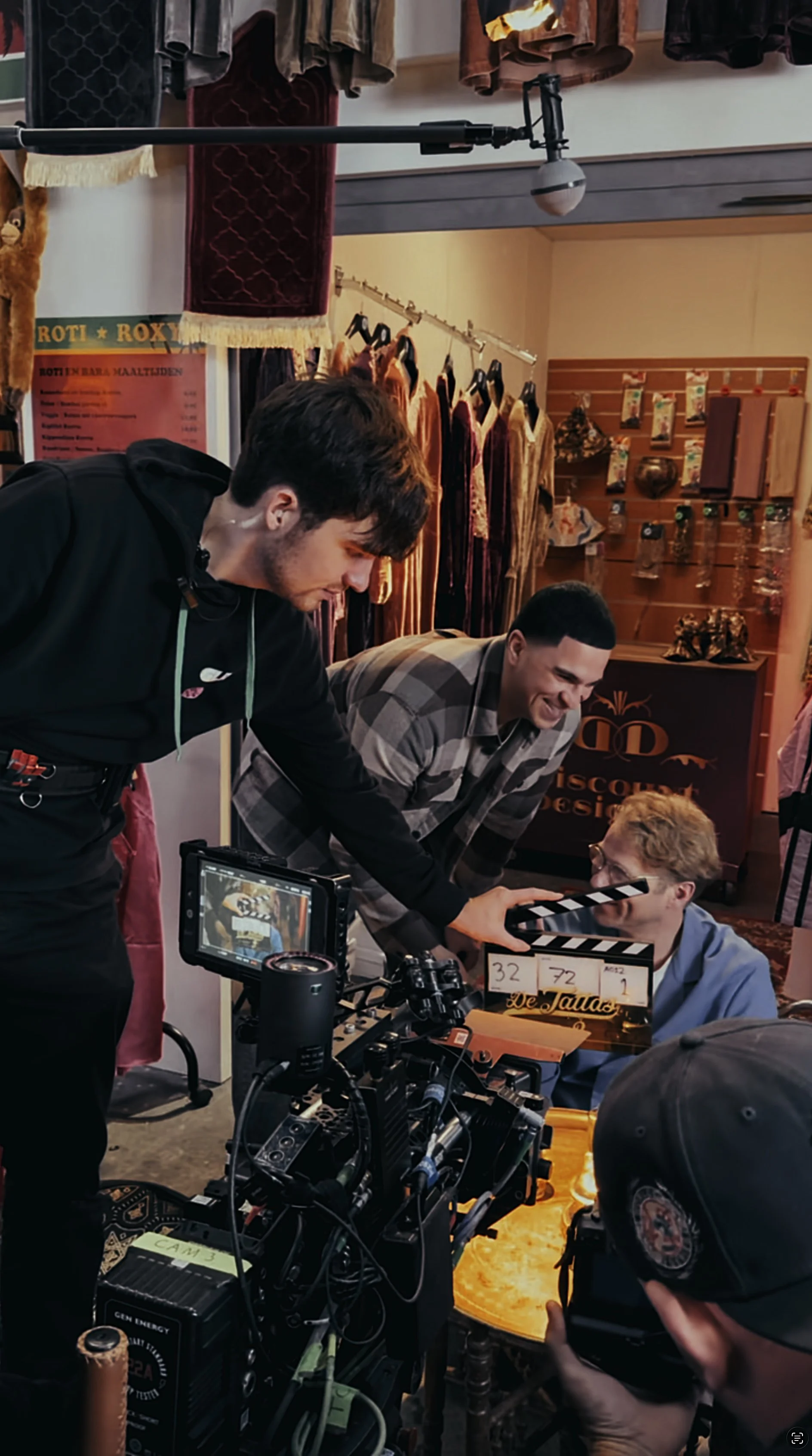 Mensen op een filmset die samenwerken, met een camera, clapperboard en kleding in de achtergrond.