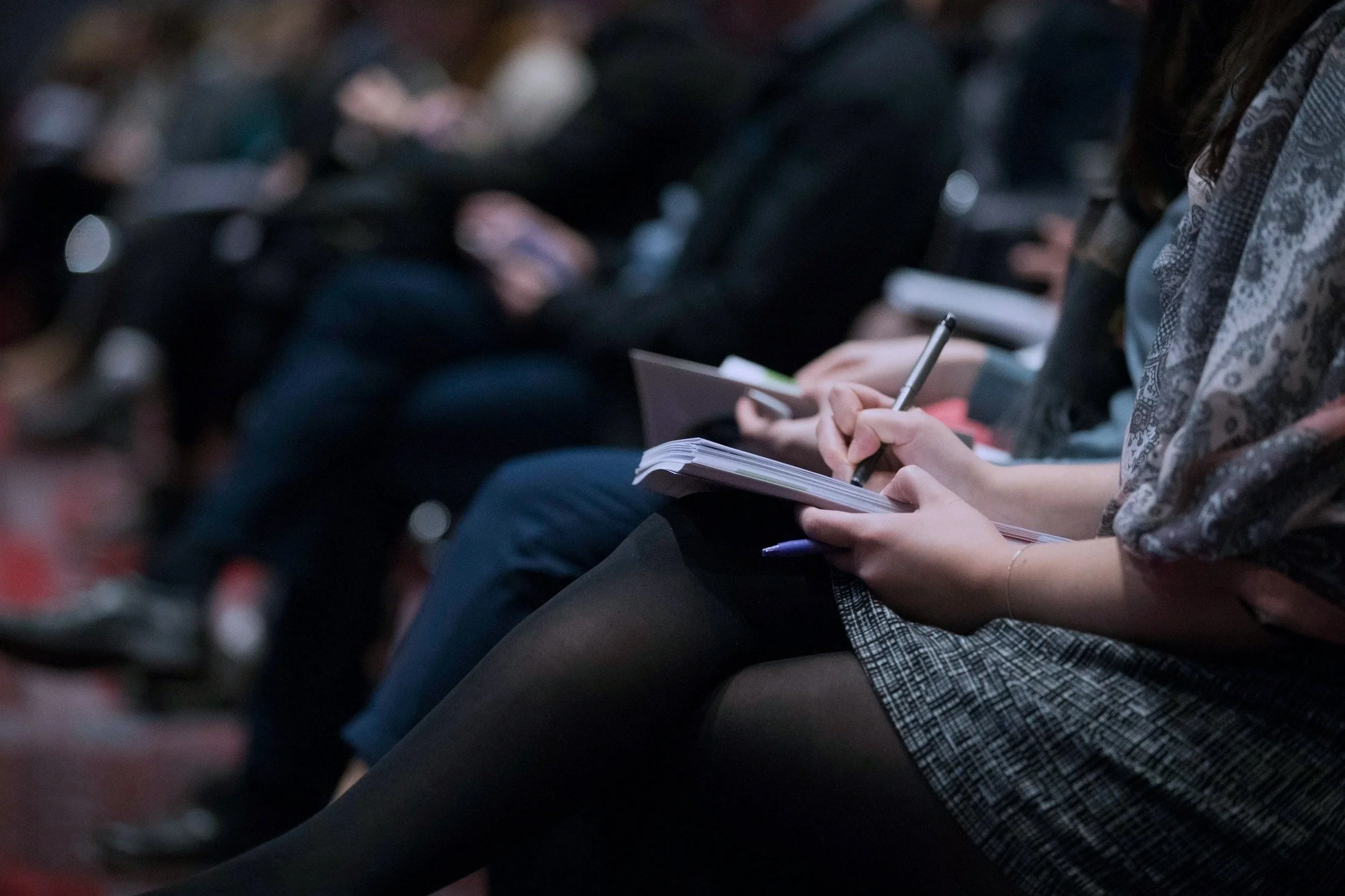 People sitting on chairs, taking notes during a conference or seminar from a sport psychology professional.