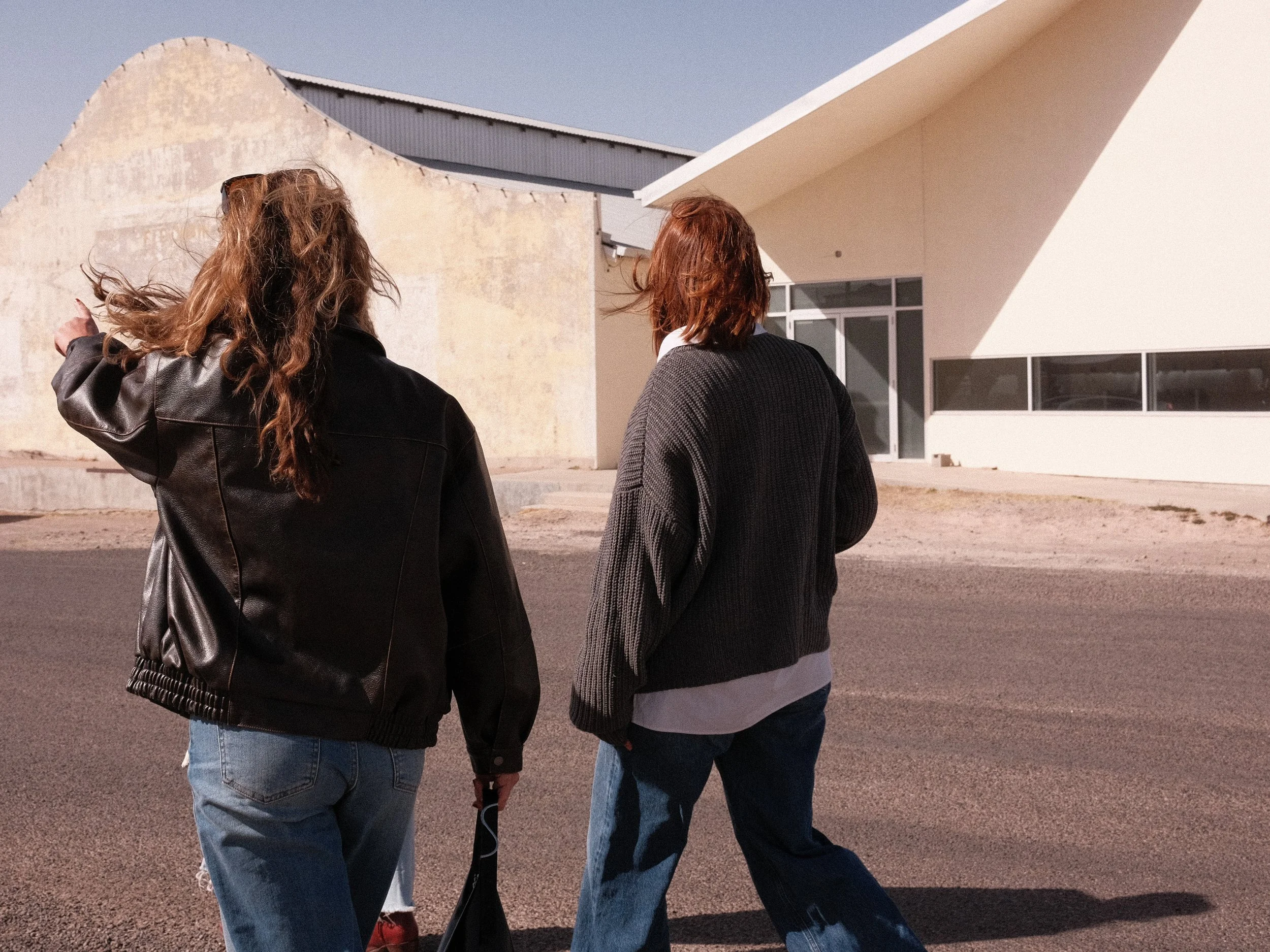 Two women walking outside near a modern building with large windows, during daytime with clear sky.