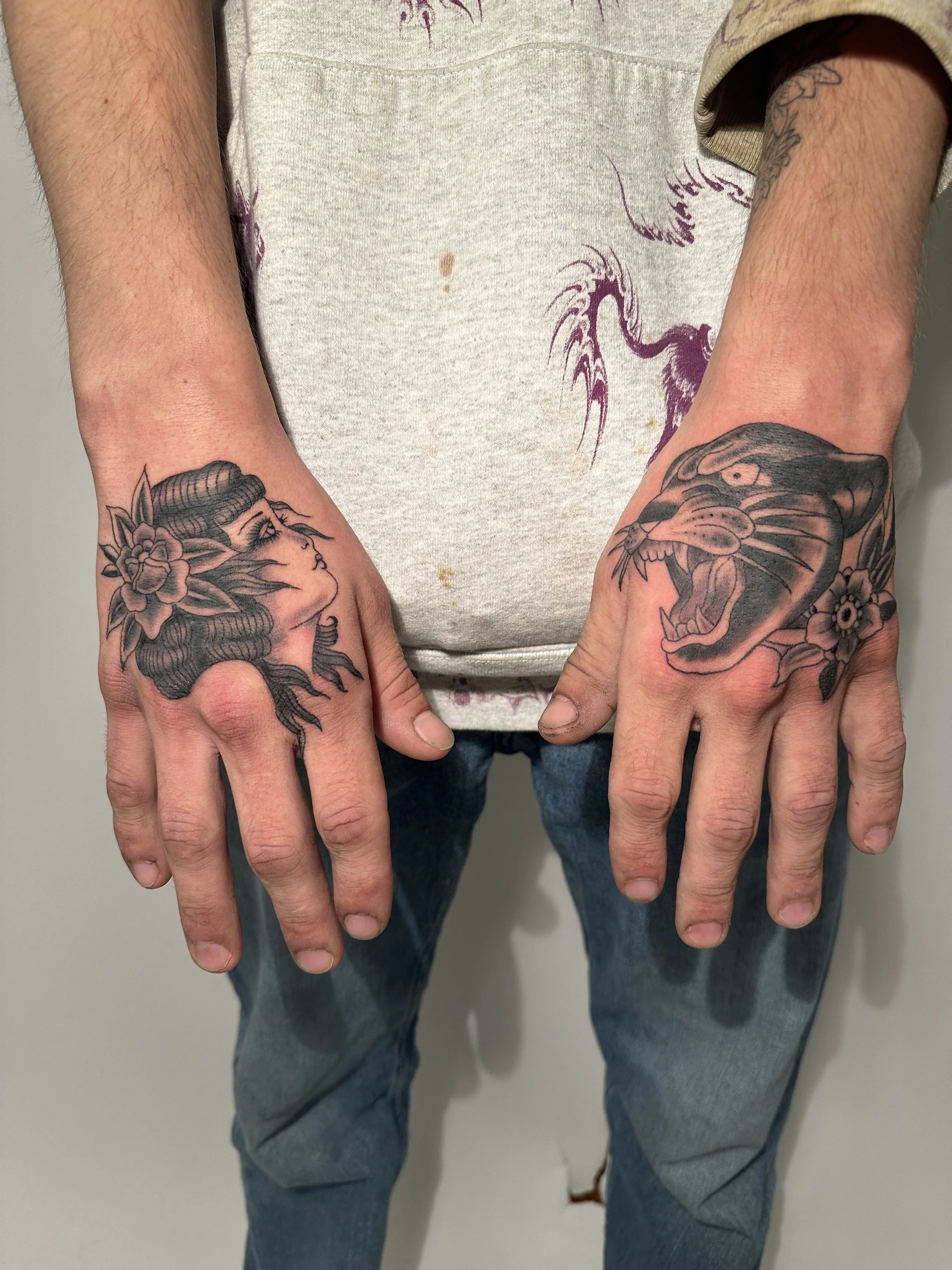 Person displaying tattoos of a woman with flowers on the left hand and a roaring panther with flowers on the right hand.