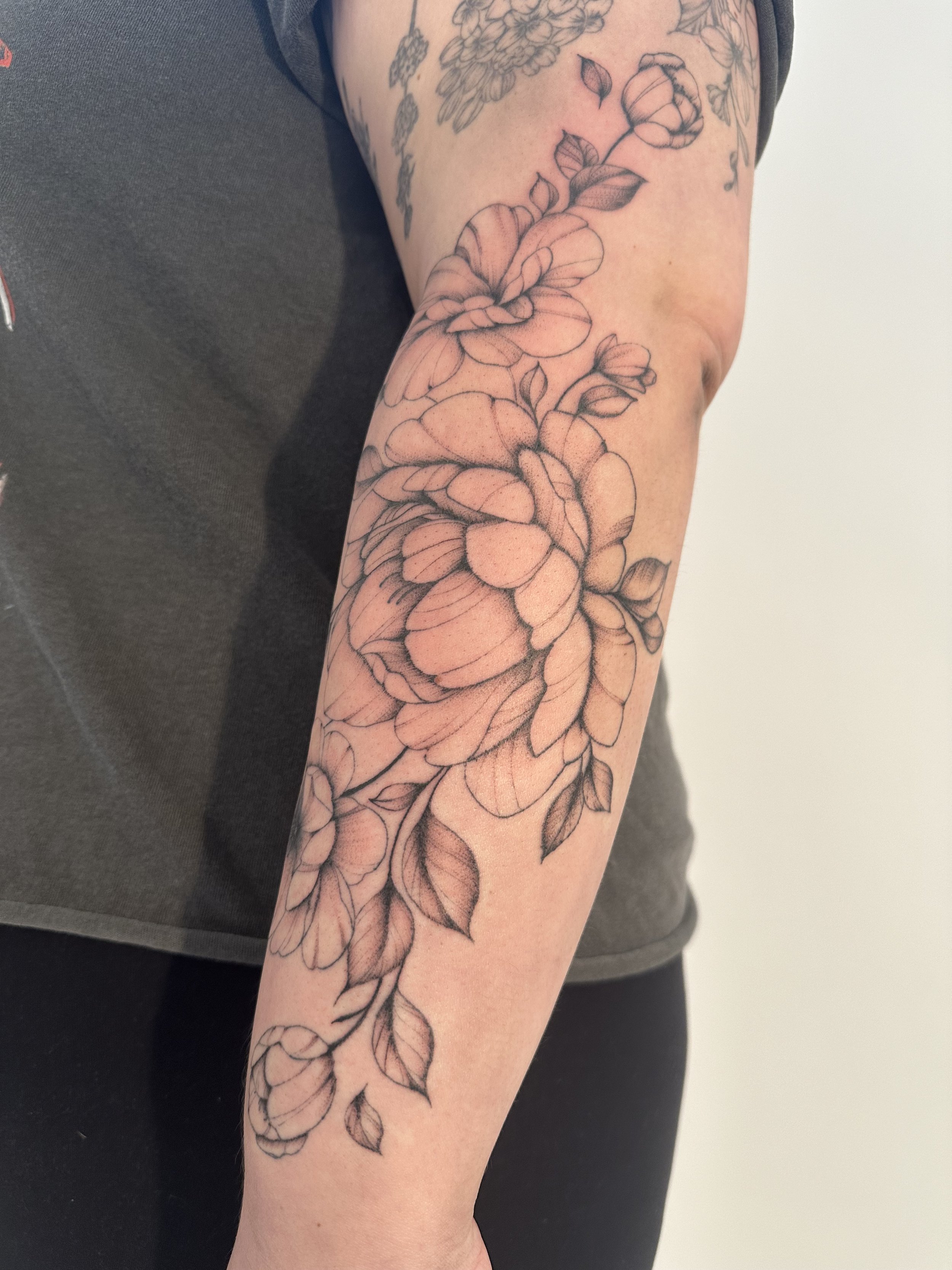 Black and gray floral tattoo on forearm, featuring large blooming roses with detailed leaves.