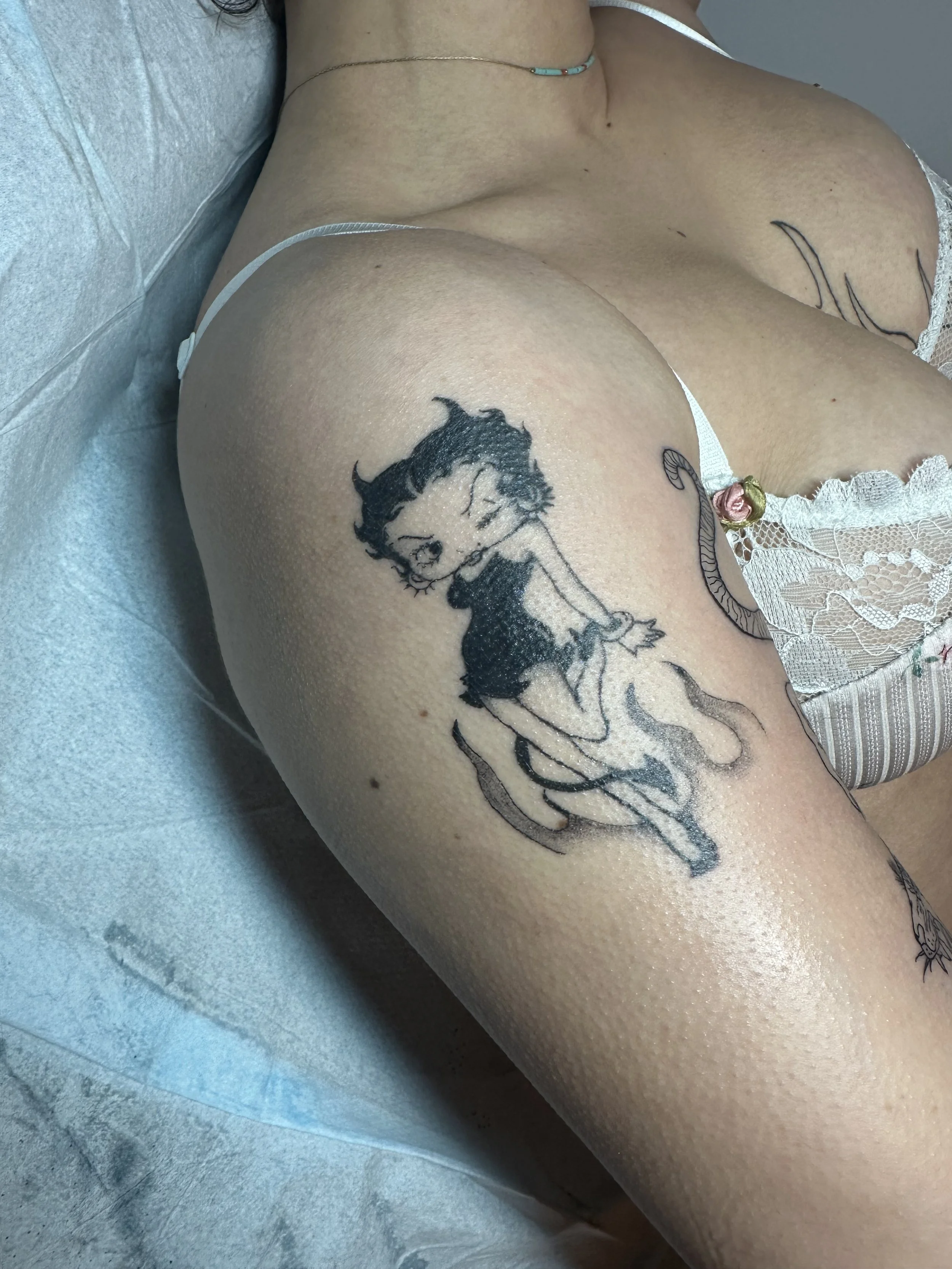 Close-up of a person's upper thigh and hip, showing a tattoo of Betty Boop sitting on a crescent moon.