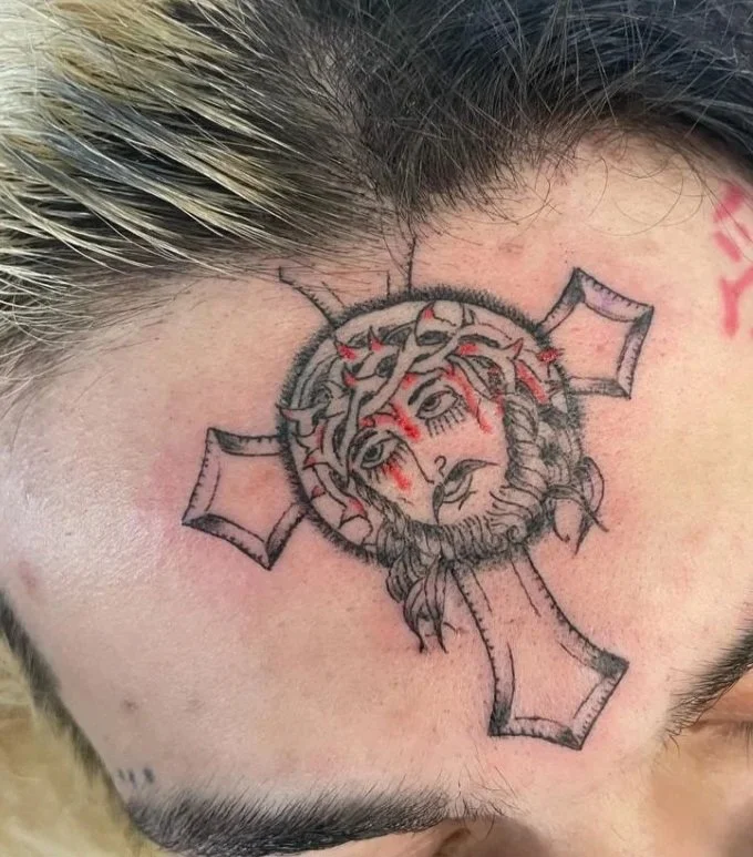 Tattoo of a woman's face with a crown of thorns, blood streaks, and a halo, with a cross shape behind her head.