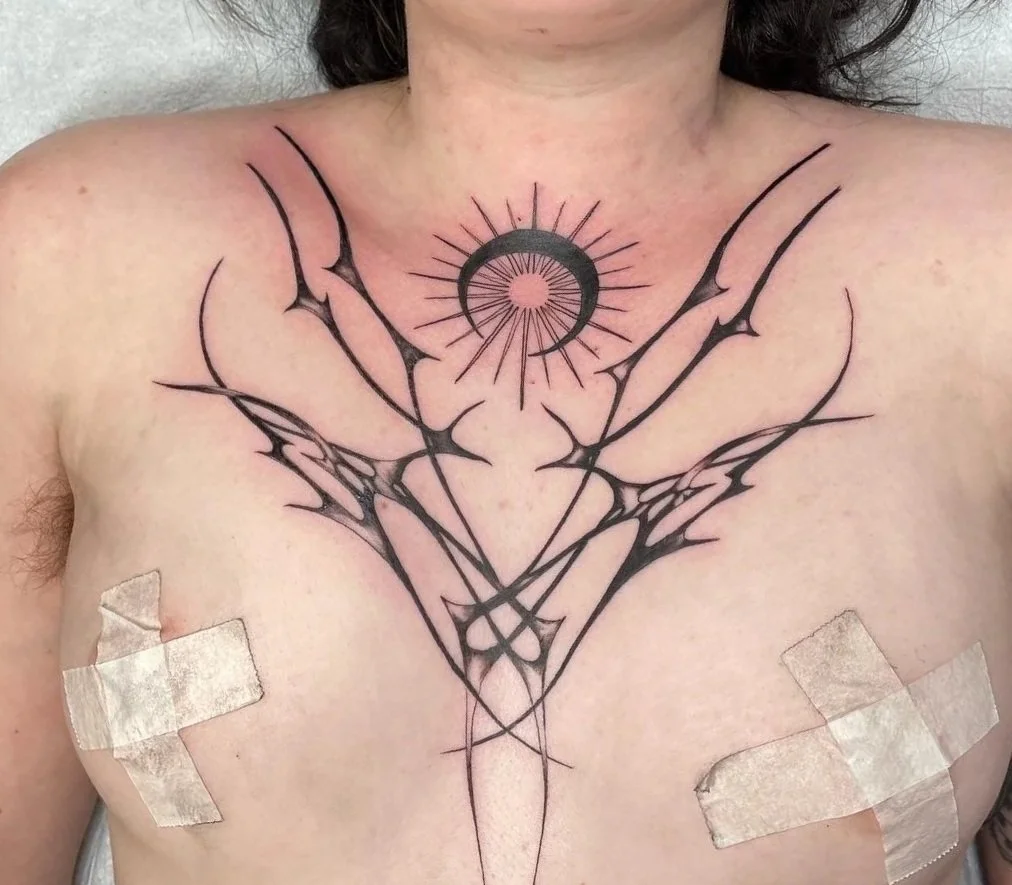 A chest tattoo featuring black abstract, geometric, and line art design with a central circle and sun rays.