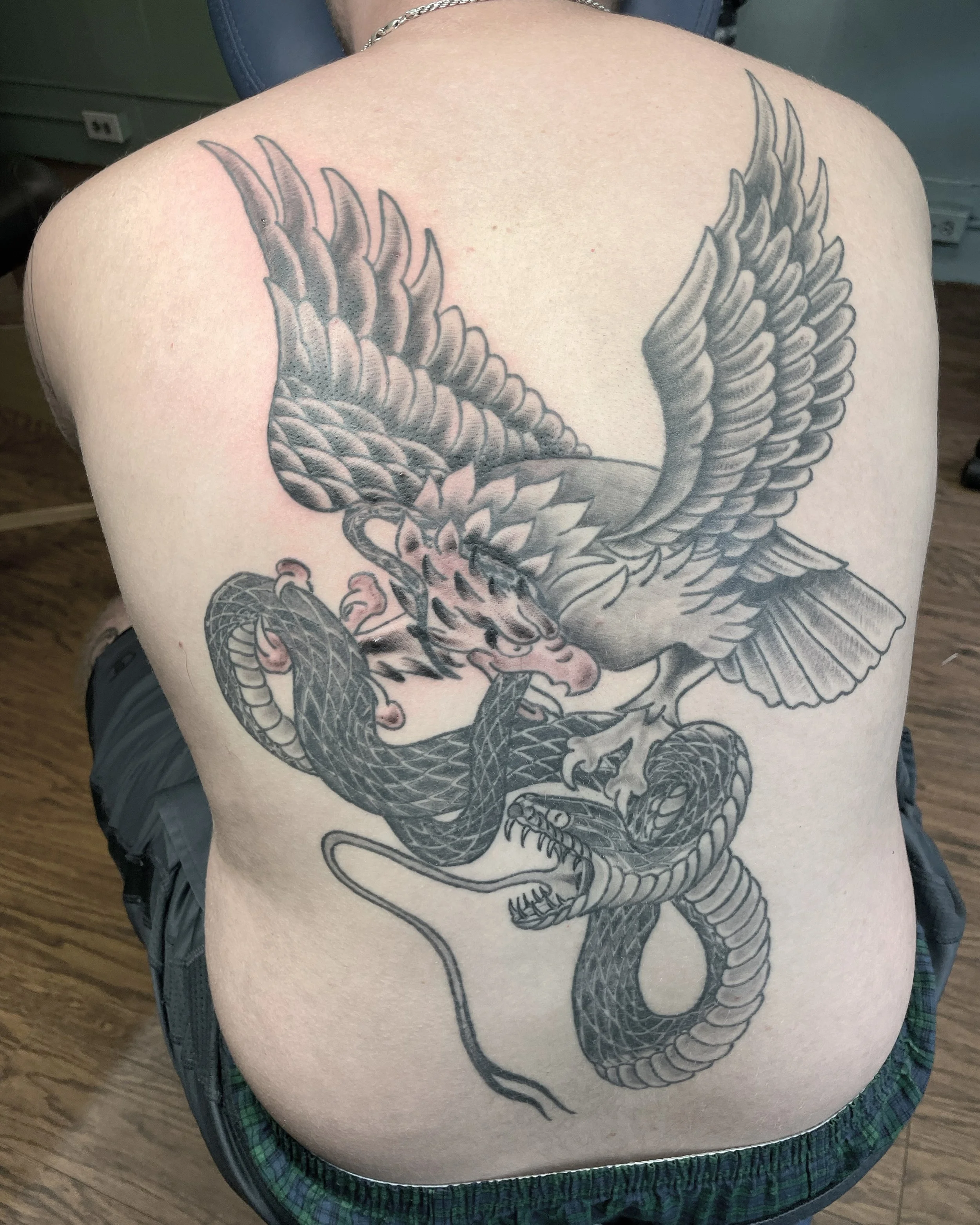 Tattoo of an eagle and a snake intertwined on person's back.