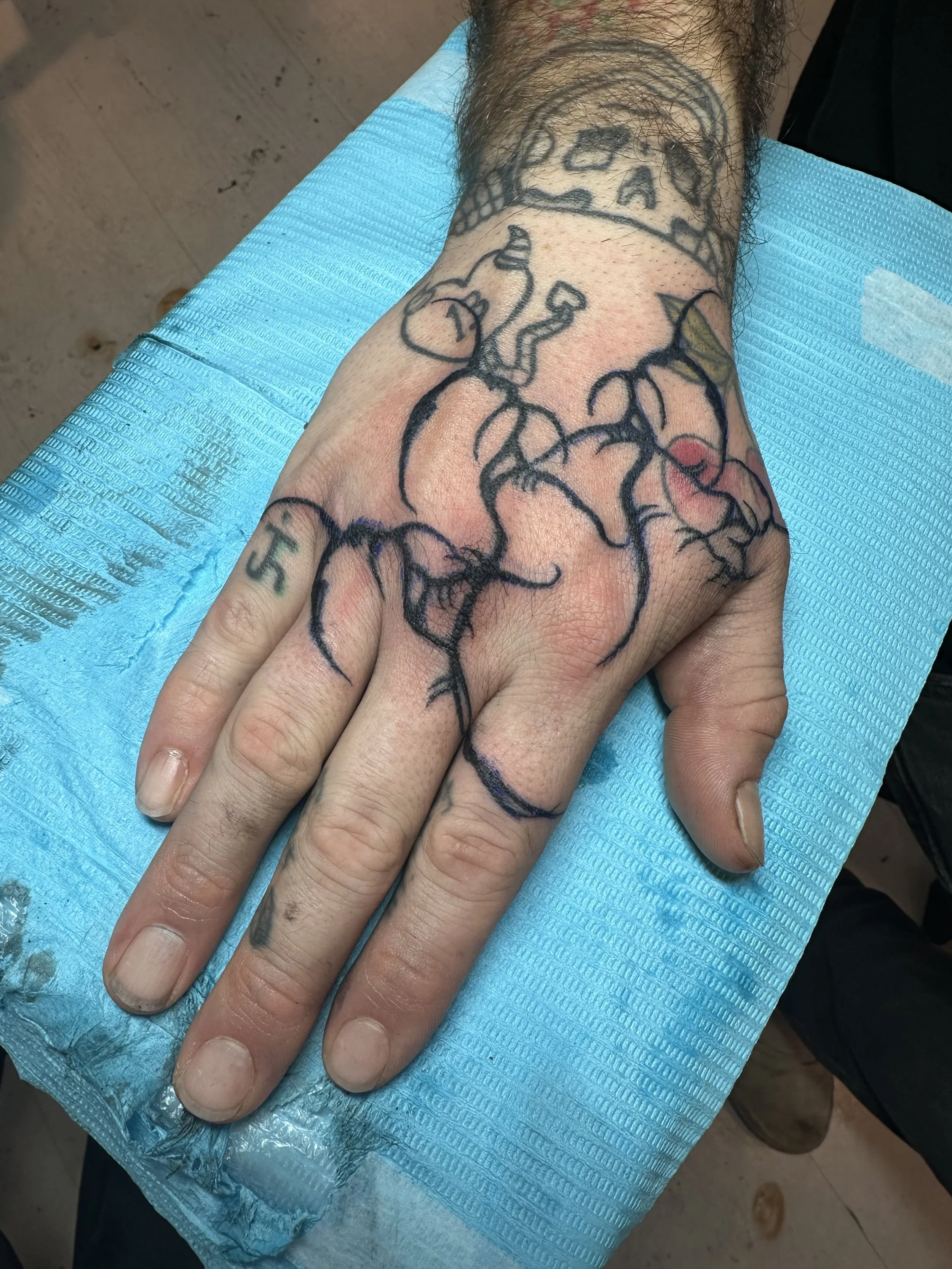 A hand with a detailed black outline tattoo of a heart with an intricate network of veins, resting on blue medical paper.