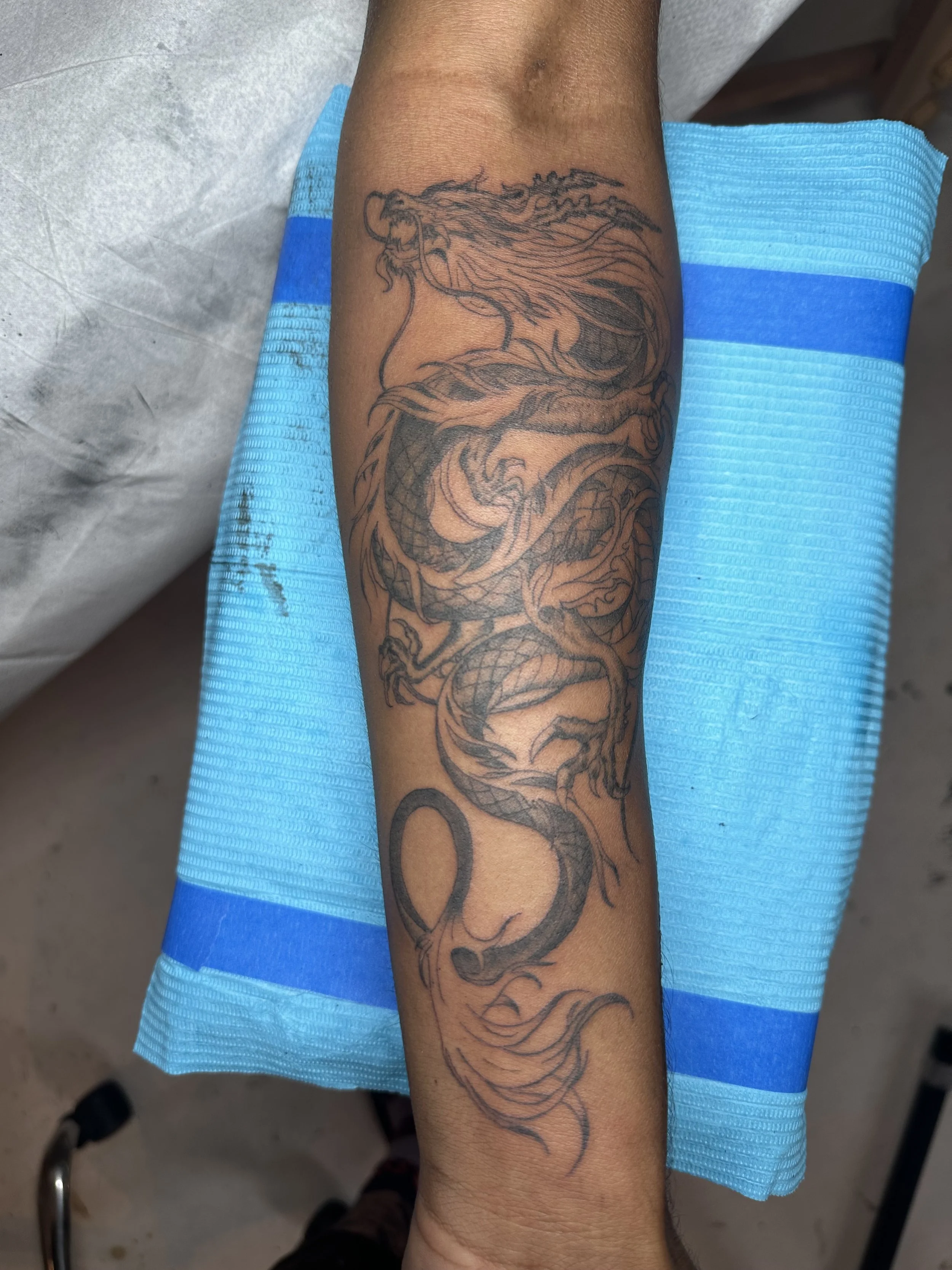 Black and gray tattoo of a dragon on a person's forearm.