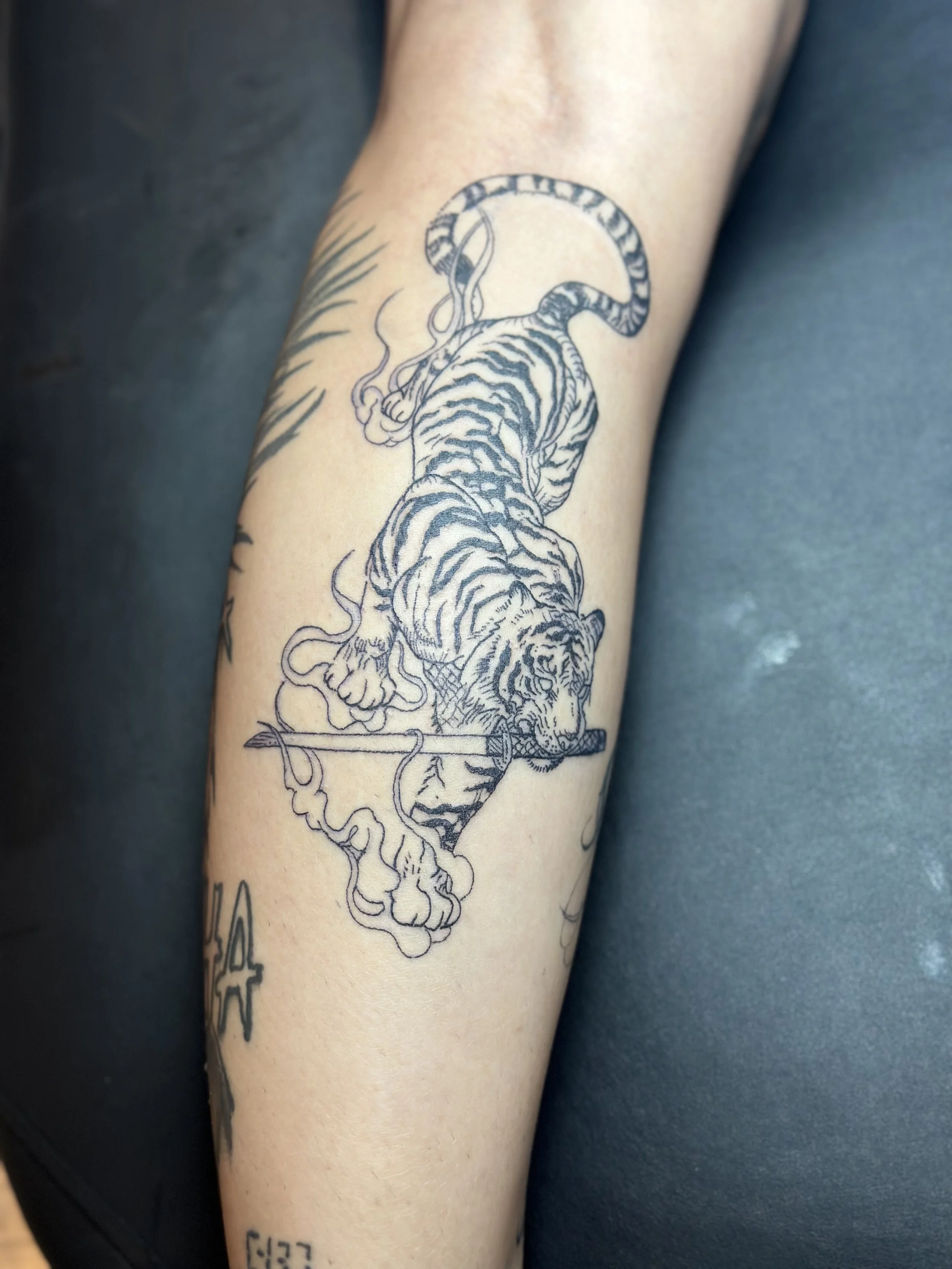 Tattoo of a tiger walking on a branch with smoke around it on a person's forearm.