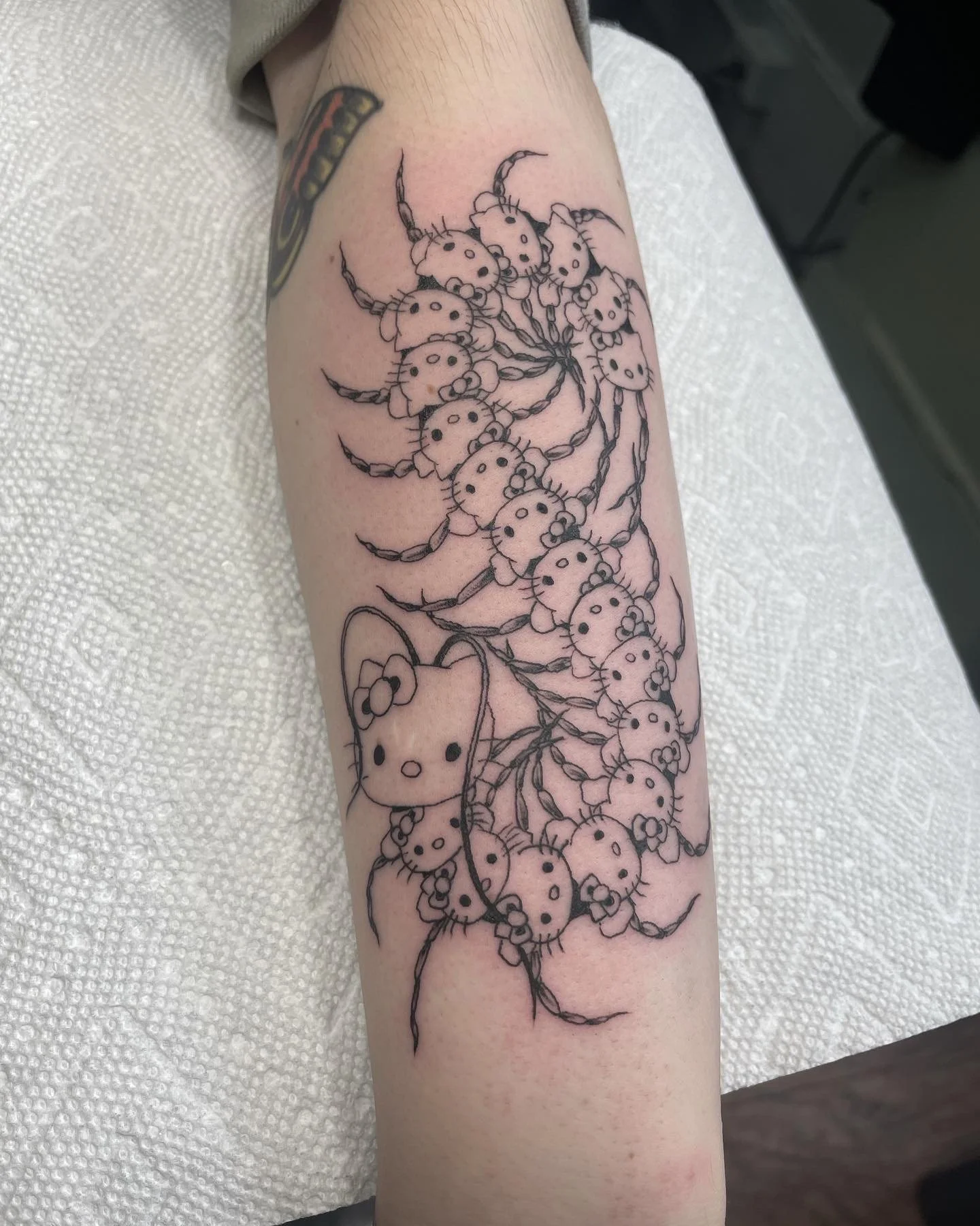 Tattoo of Hello Kitty characters forming a floral design on a person's forearm.