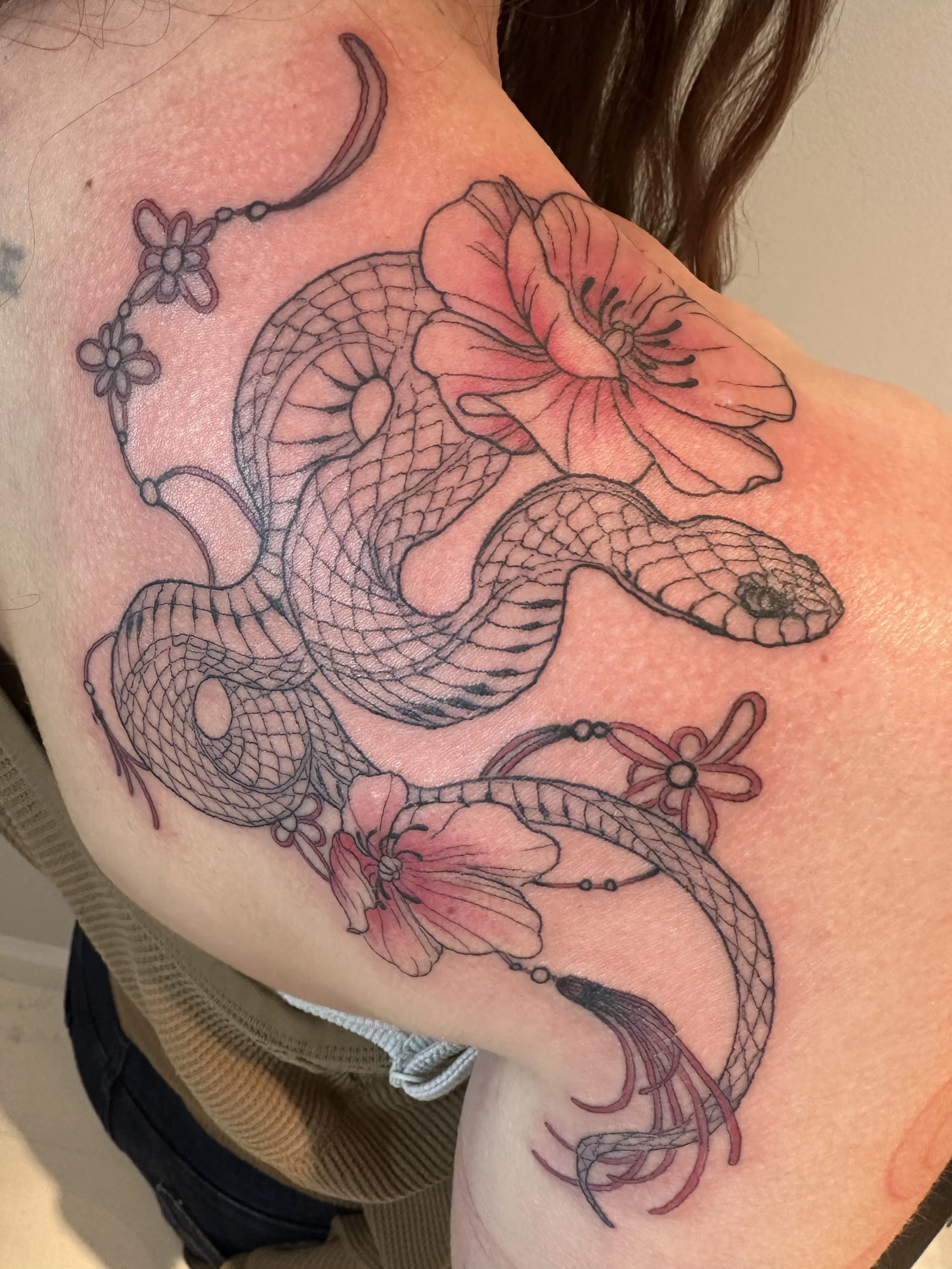 A tattoo of a snake intertwined with pink flowers on a person's shoulder.