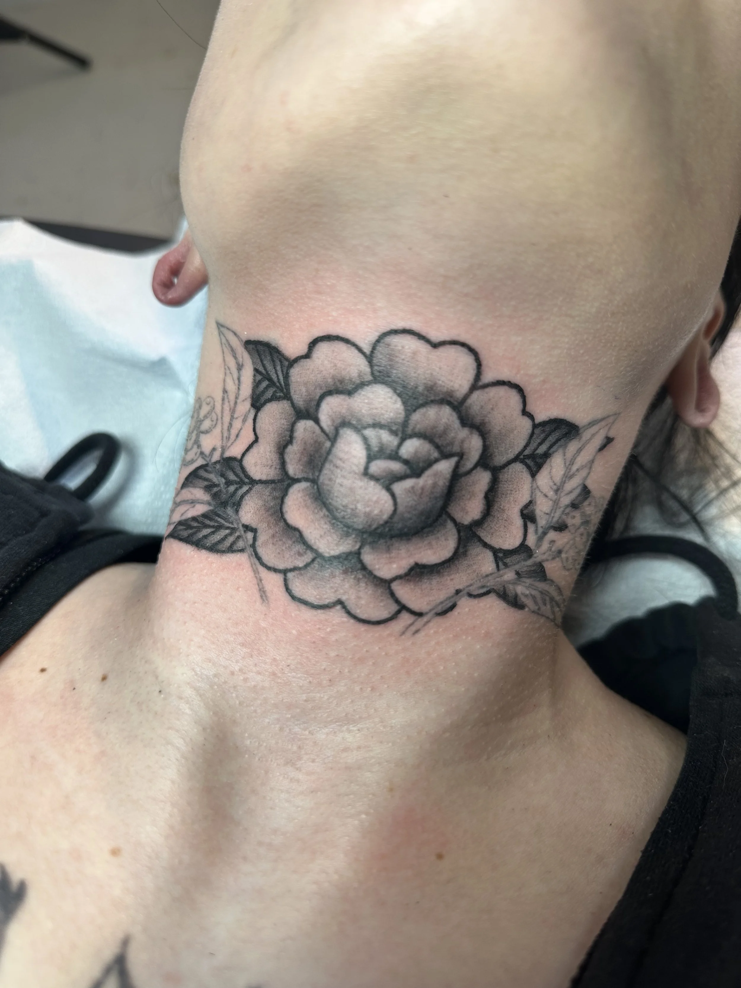 Black and gray tattoo of a large flower with leaves on the neck of a person.