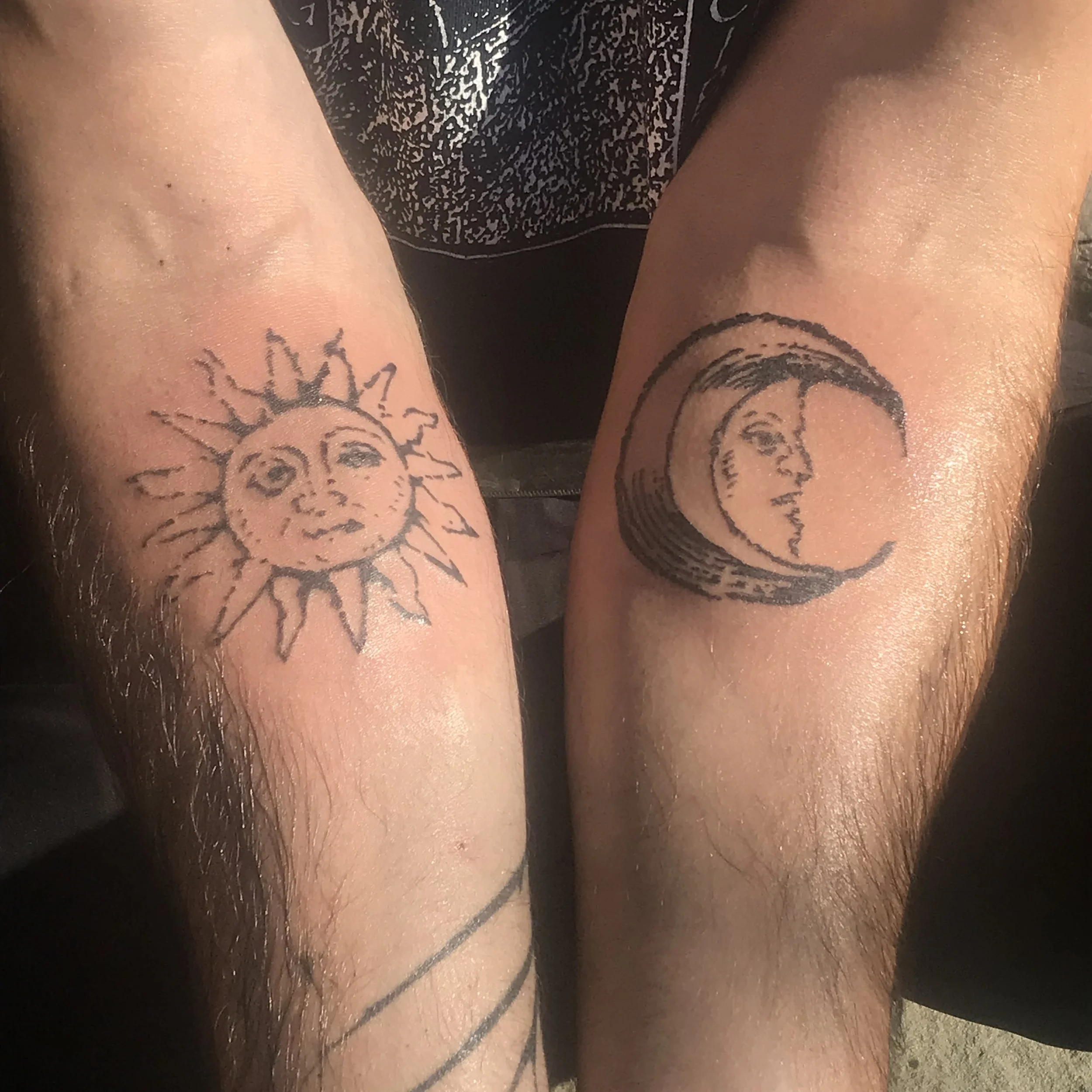 Tattoo of a smiling sun on the left arm and a crescent moon with a face on the right arm.