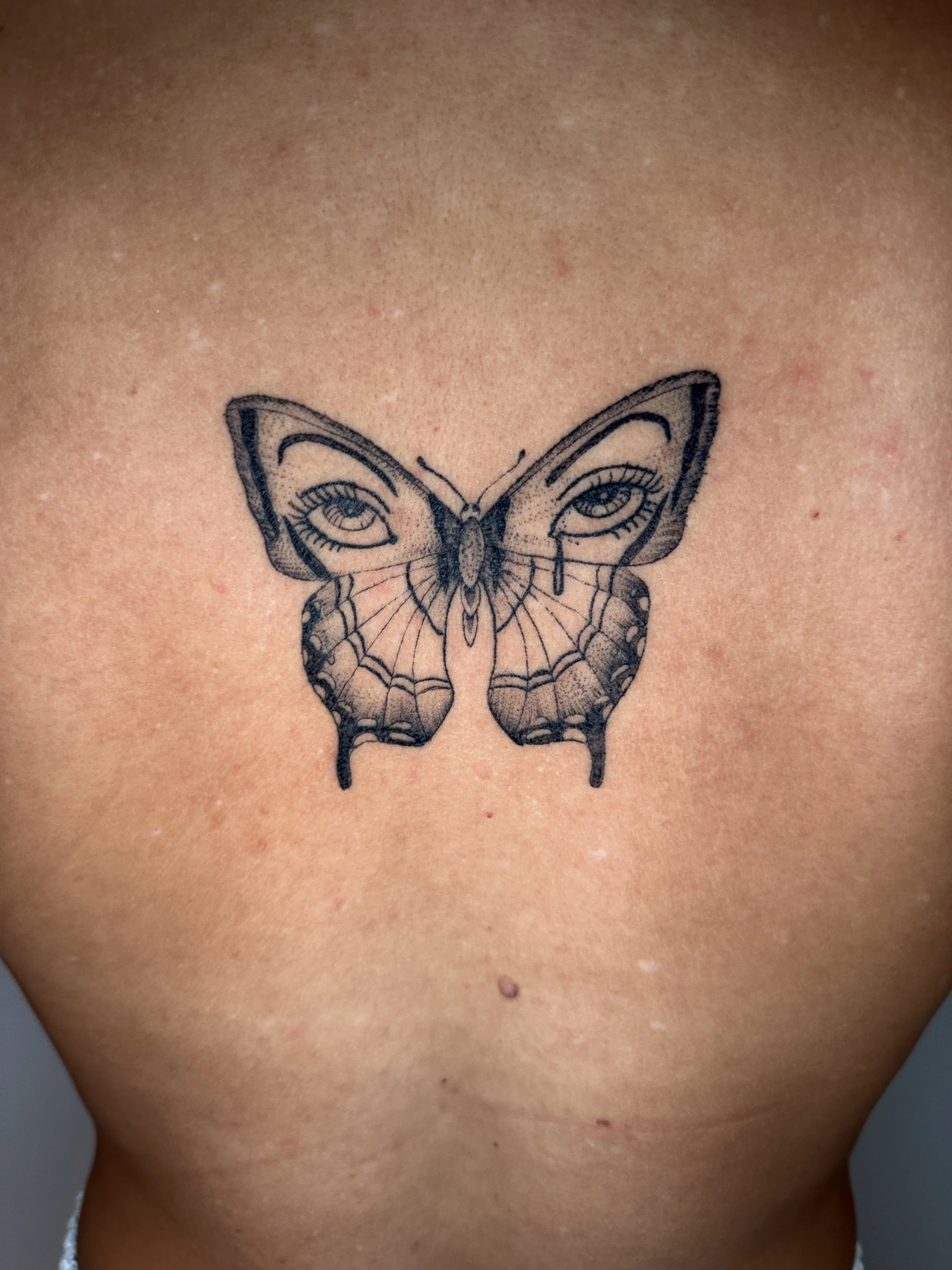 Tattoo of a butterfly on a person's chest, with detailed wings and eye designs.