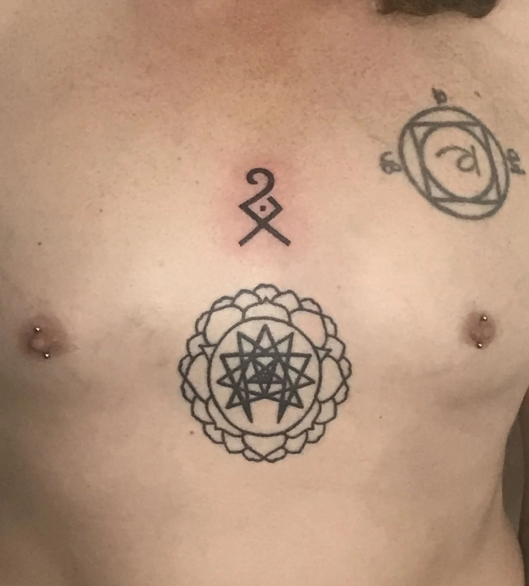New tattoos on a person's chest, including geometric and symbolic designs.