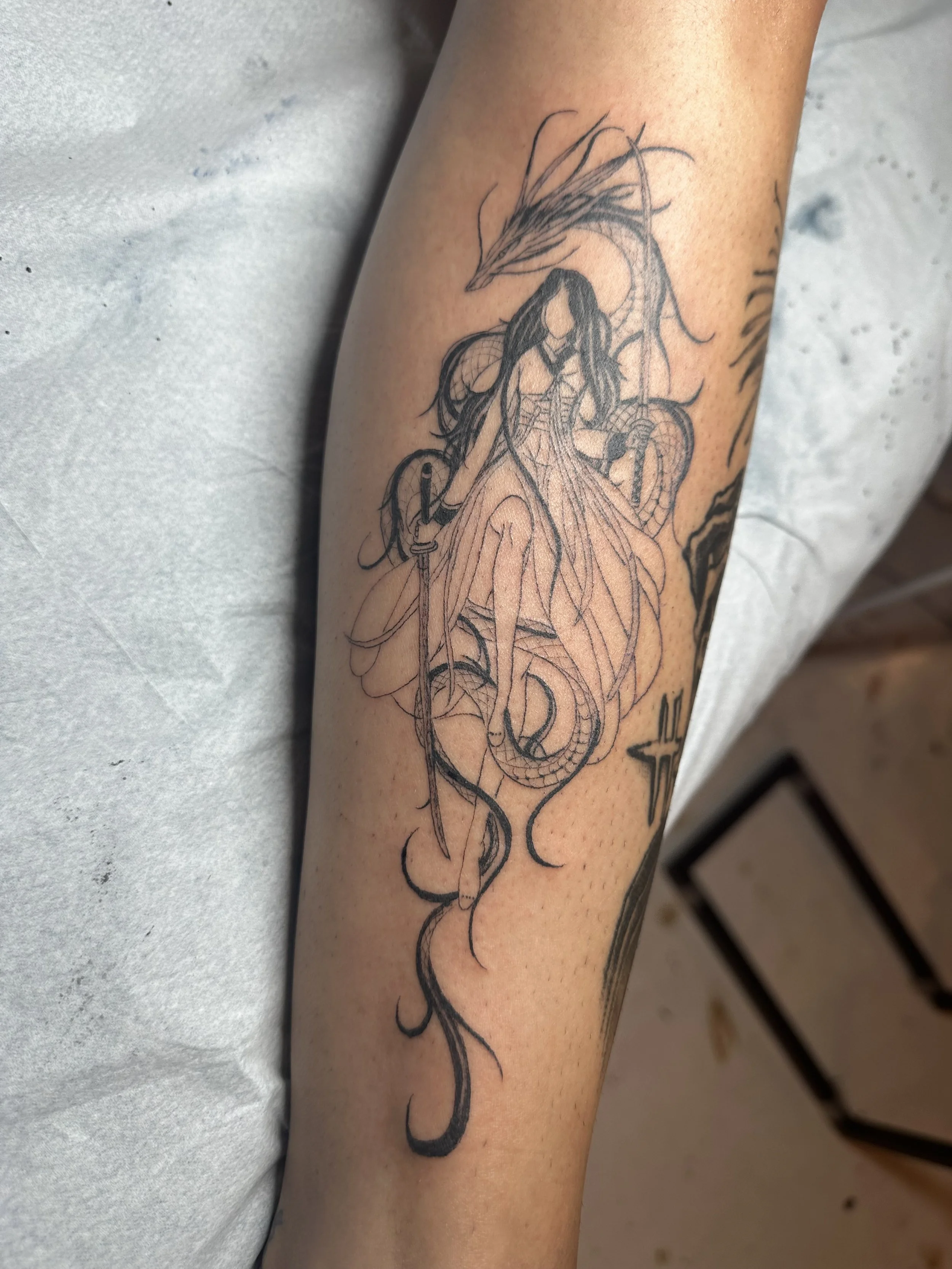 Tattoo of a female figure with long hair, holding a spear, sitting on a dragon, with a winged helmet and scales on her gown.