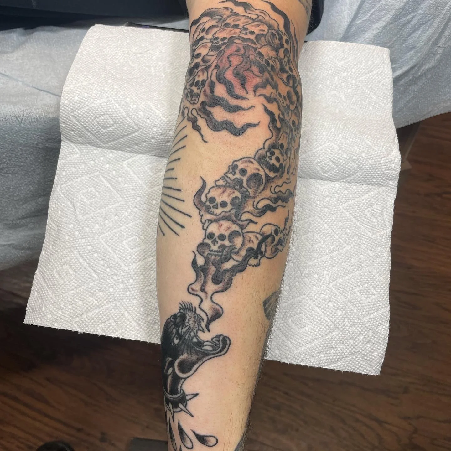 Tattoo of skulls and smoke on person's forearm, with a lion's head at the bottom.