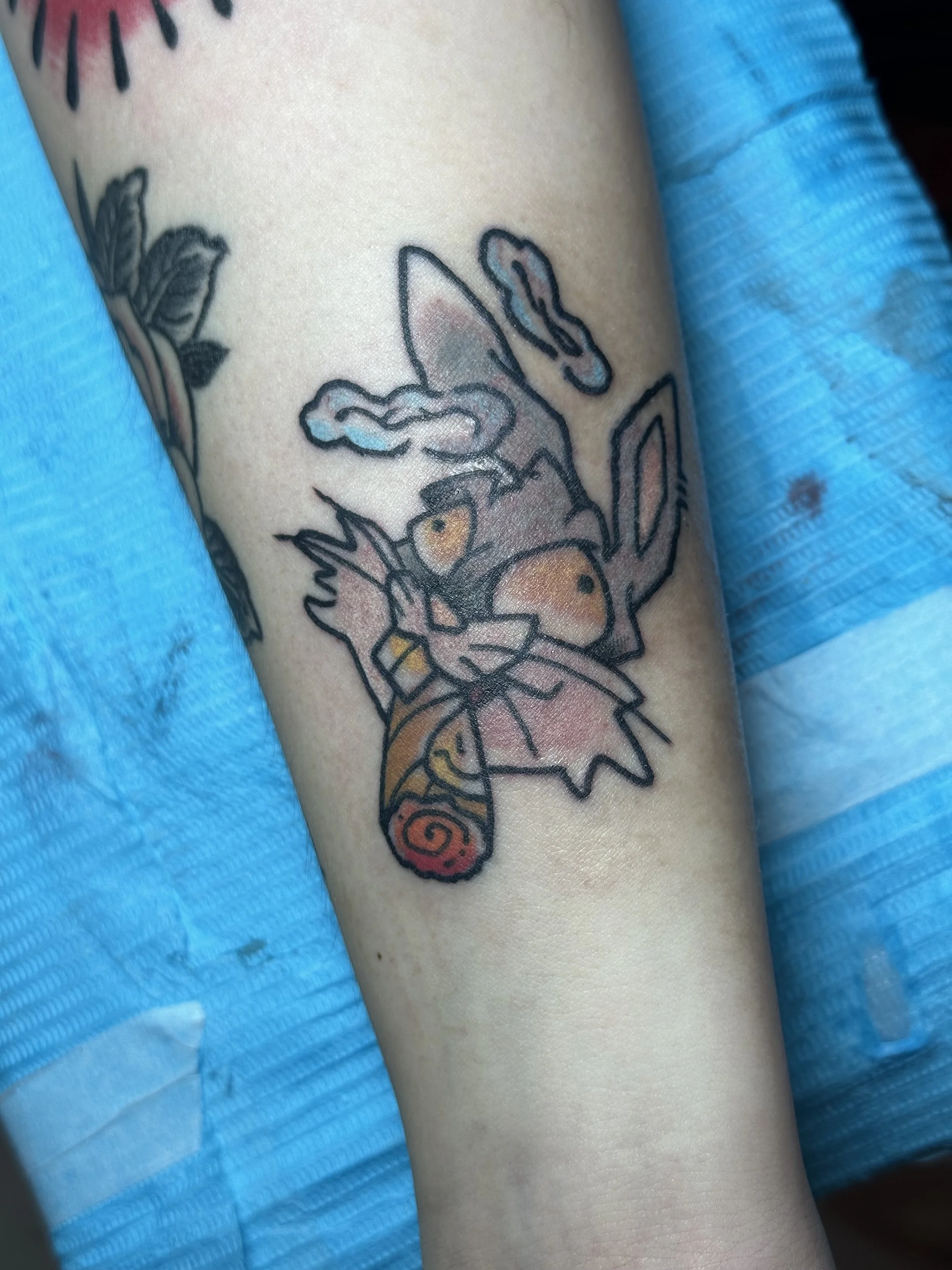 Tattoo of Eevee from Pokémon with a leaf, cloud, and swirl design on a person's arm.