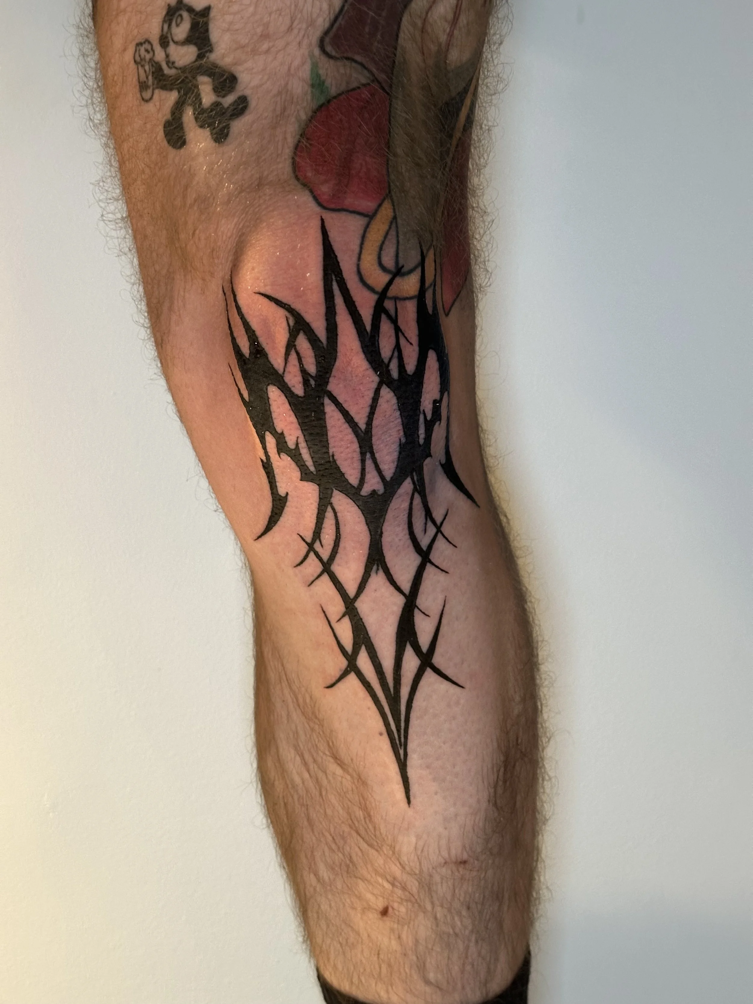 Tattoo of a black tribal-style design on a person's thigh, with other tattoos visible on the upper thigh and hip area.