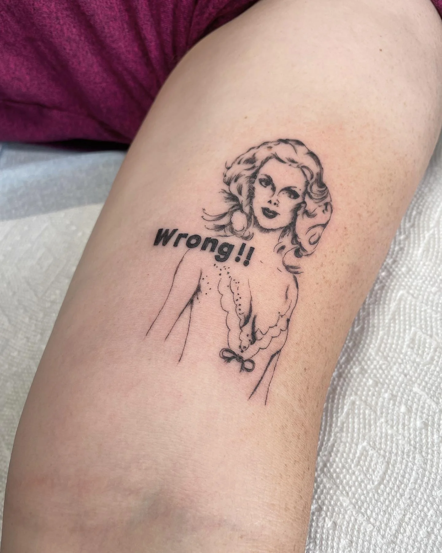Tattoo of a woman with wavy hair and lipstick, with the word "Wrong!!" next to her.