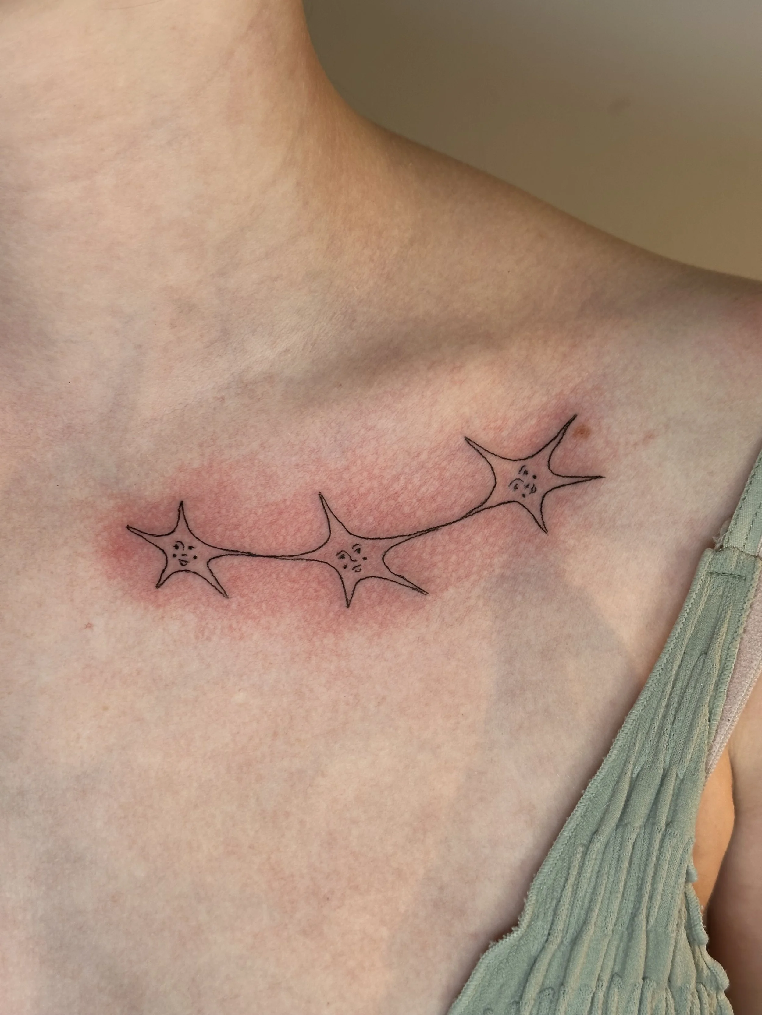 Tattoo of three sad-looking starfish on the upper chest.