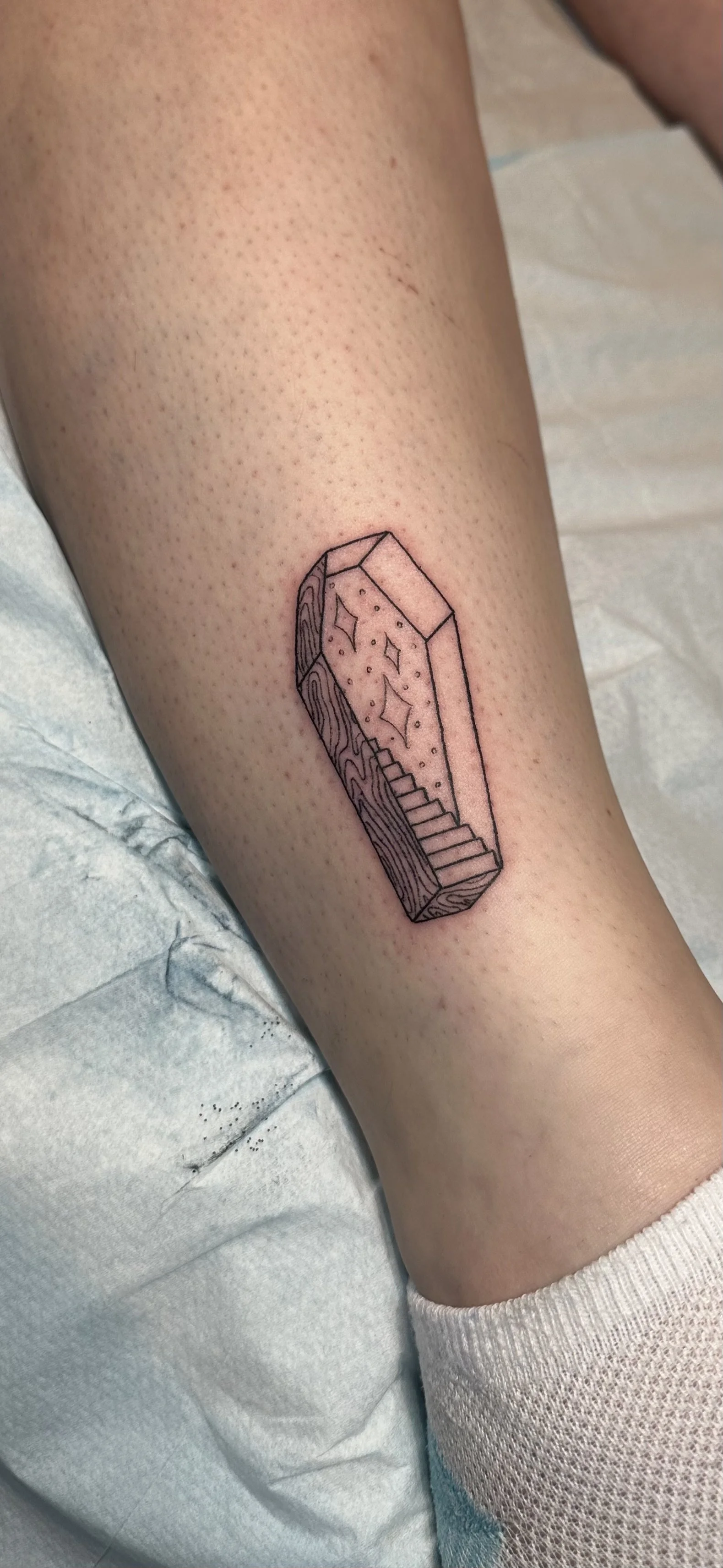 A new tattoo of a geometric, outlined crystal with a staircase on its side, inside. The interior of the crystal contains stars and small dots.