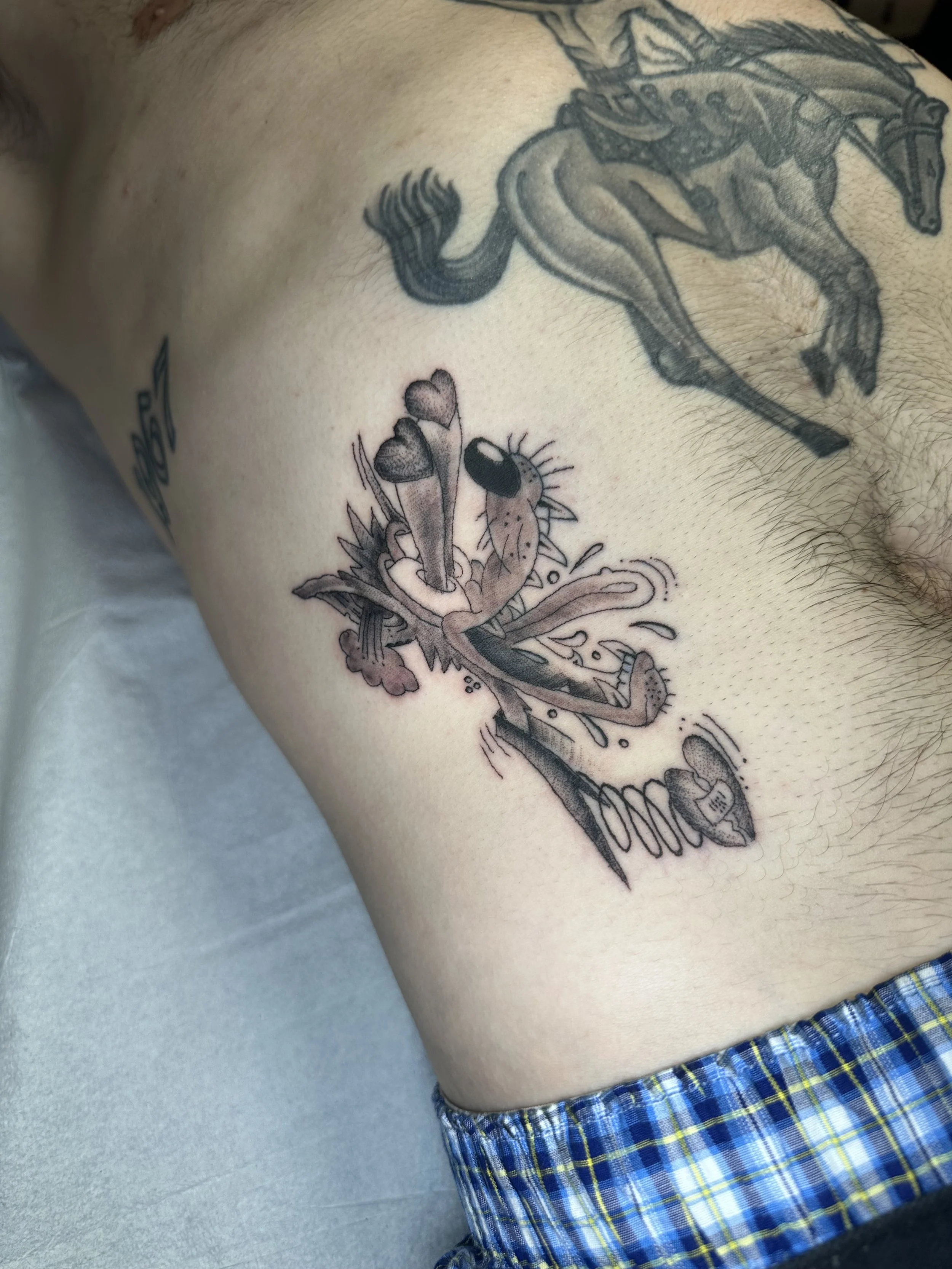 Tattoo of a cartoonish dog with a spring in its mouth and two hearts on its tongue, in a stylized, comic art style.