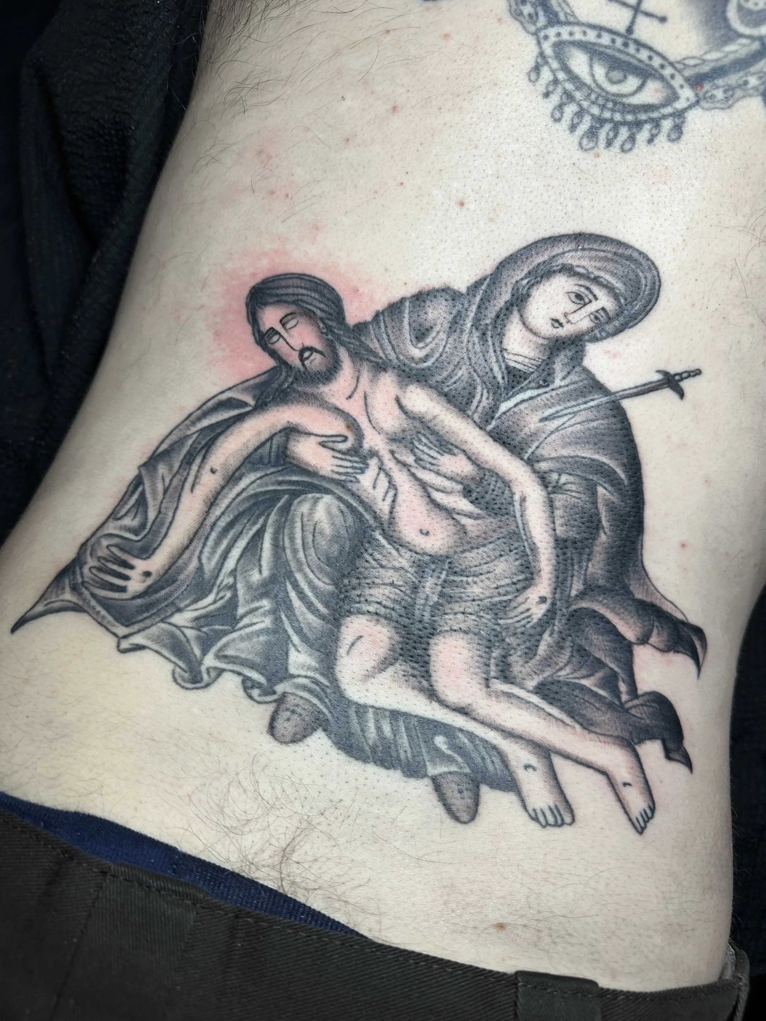 Tattoo of the Pietà, depicting the Virgin Mary holding the body of Jesus Christ after the crucifixion, rendered in black ink with detailed shading.