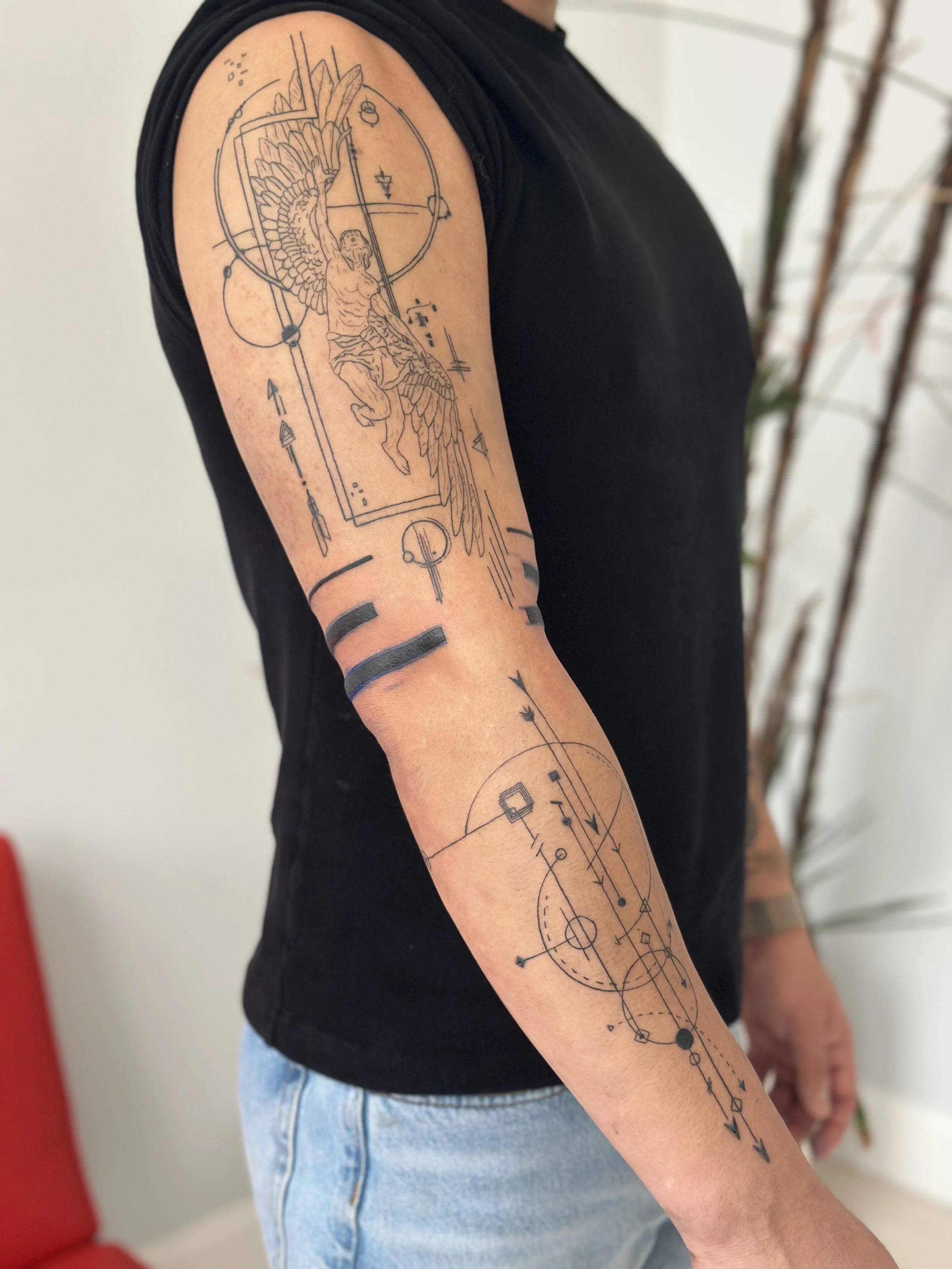 Tattoo of a winged figure on the upper arm with intricate geometric and celestial designs.
