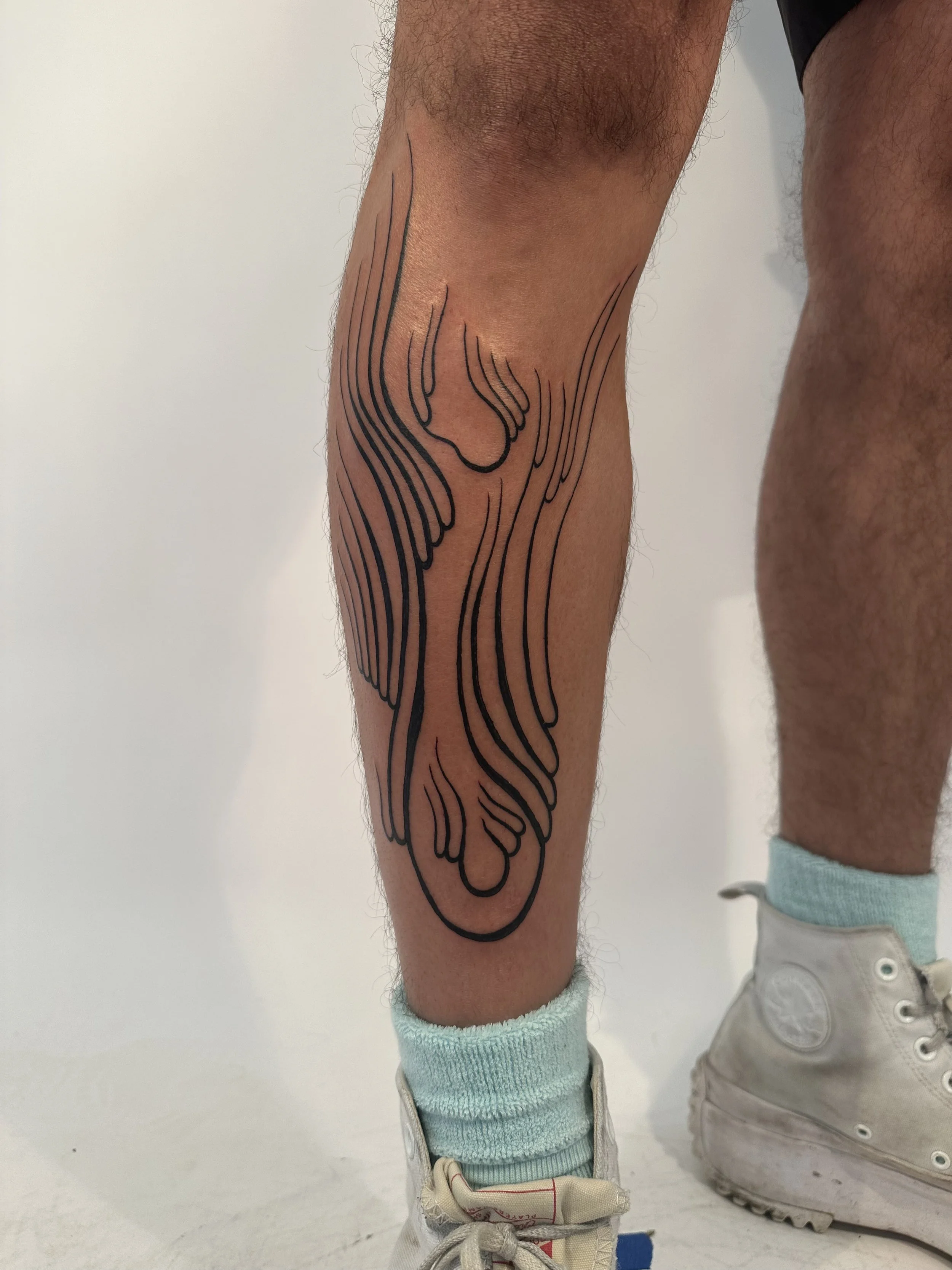 A person's lower leg with a large, black, abstract line tattoo extending from the knee to the ankle.