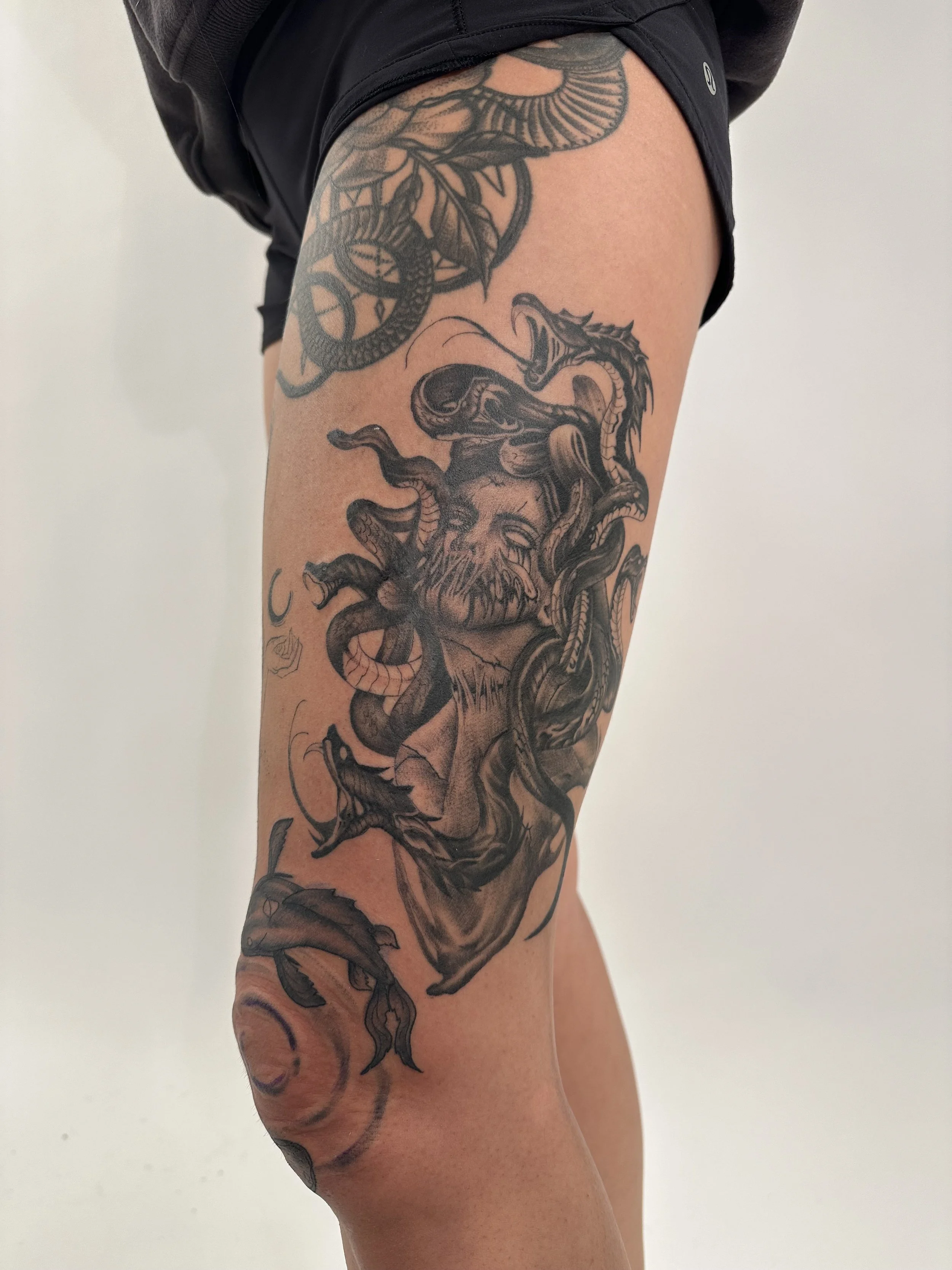 Tattoo of a face with long hair surrounded by snakes on a person's thigh and upper leg.