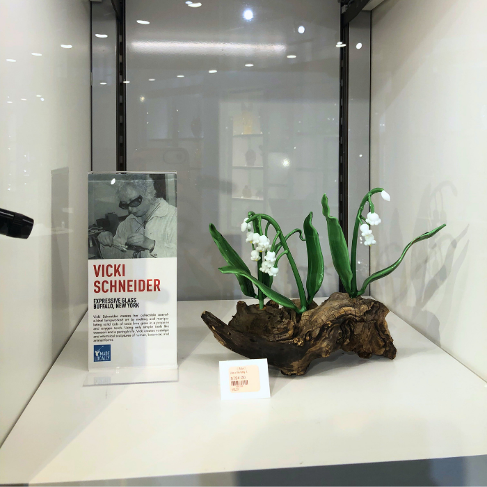 Display case featuring a black and white photo of Vicki Schneider and a floral arrangement with white flowers and green leaves in a piece of driftwood.