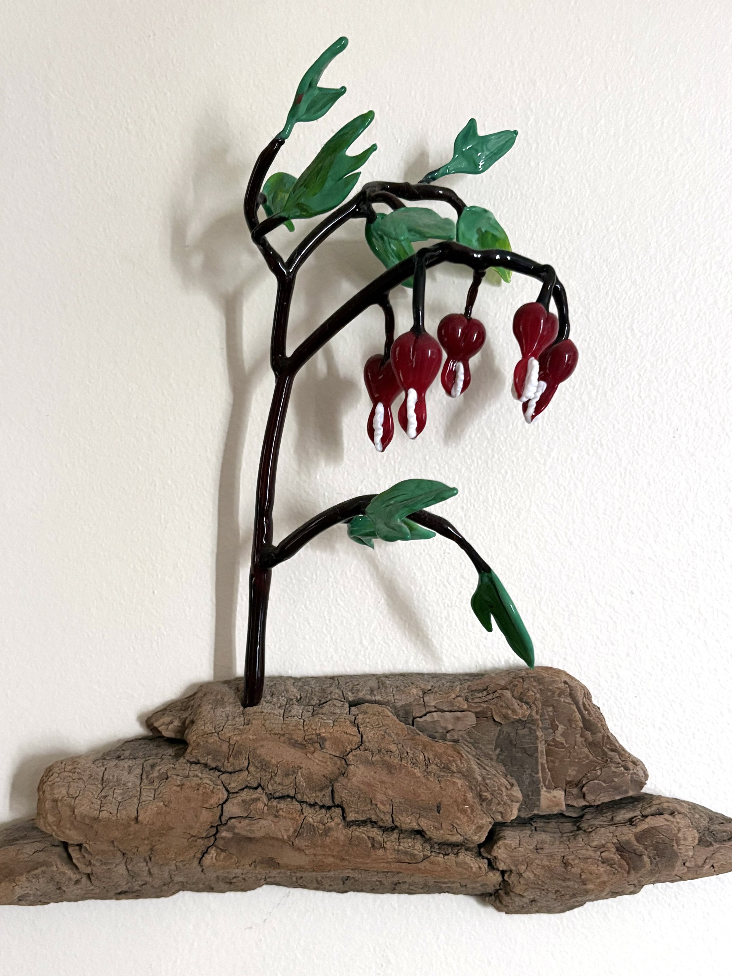 Decorative metal sculpture of a plant with green leaves and red berries, mounted on a piece of driftwood.